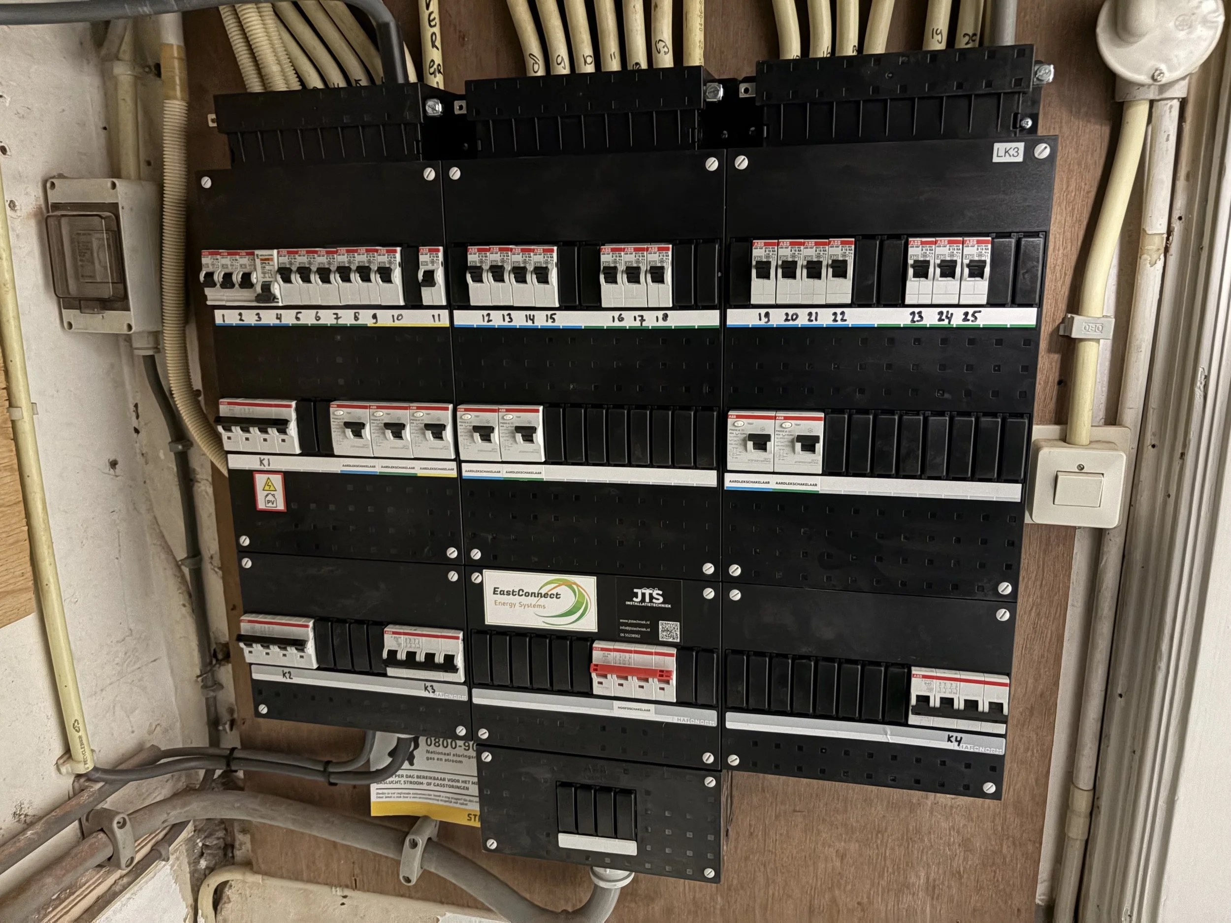Elektriciteitskast met schakelaars en draden geïnstalleerd op een houten paneel, met labels en een logo voor EastConnect Energy Systems.
