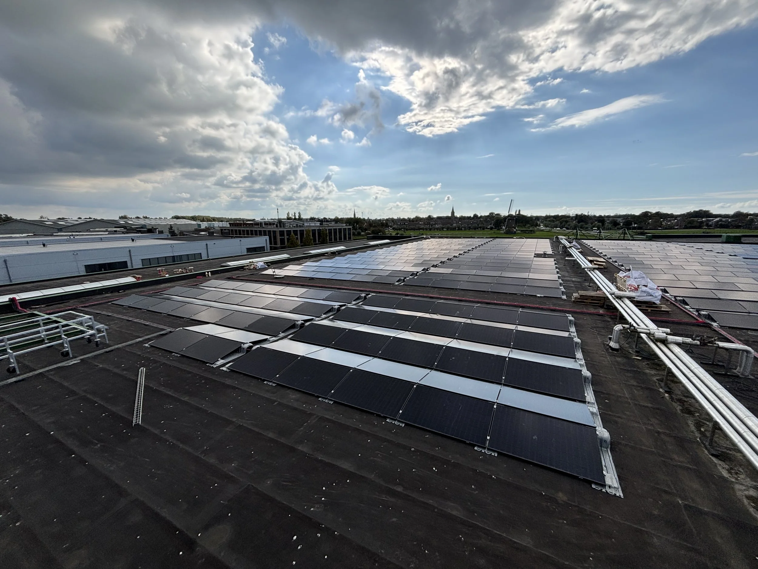 Zonnepanelen geïnstalleerd op het dak van een industrieel of kantoorgebouw, met een ondergaande zon en deels bewolkte hemel op de achtergrond.