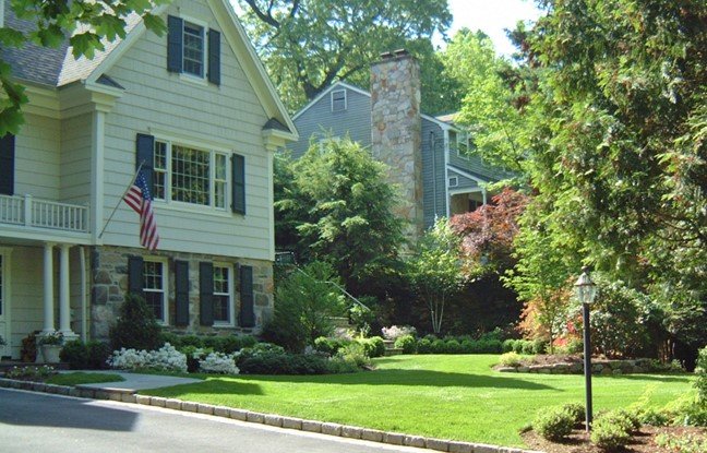 Front yard of a house with well-maintained green lawn, trees, bushes, and a lamppost