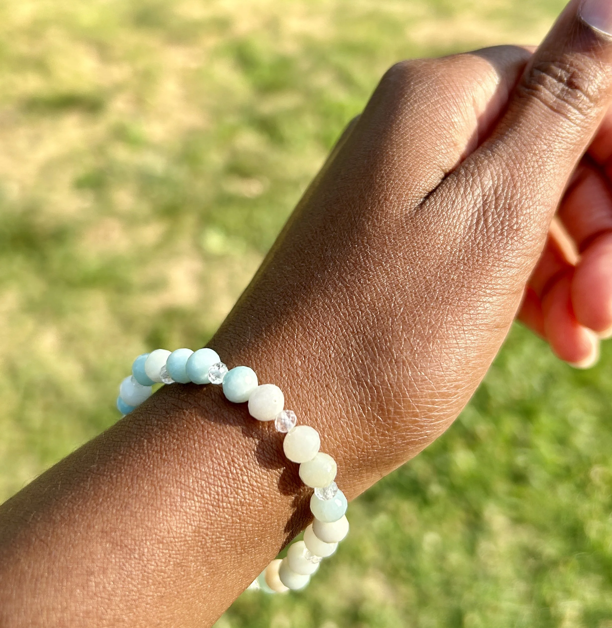 Close-up of a person's hand wearing a pastel-colored beaded bracelet, with a grassy background.