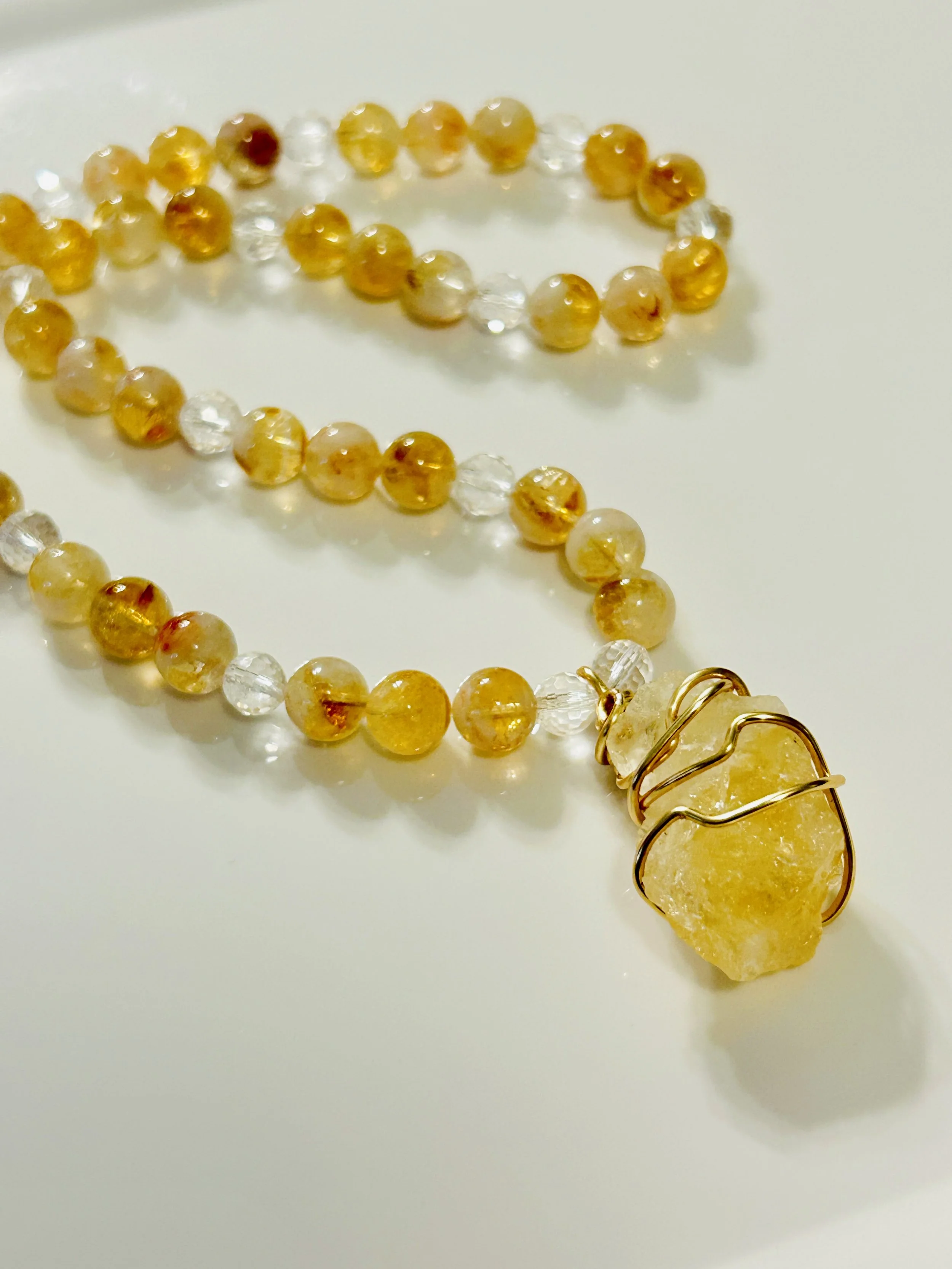 Beaded necklace with yellow and clear beads, featuring a large yellow stone pendant wrapped in gold wire on a white background.