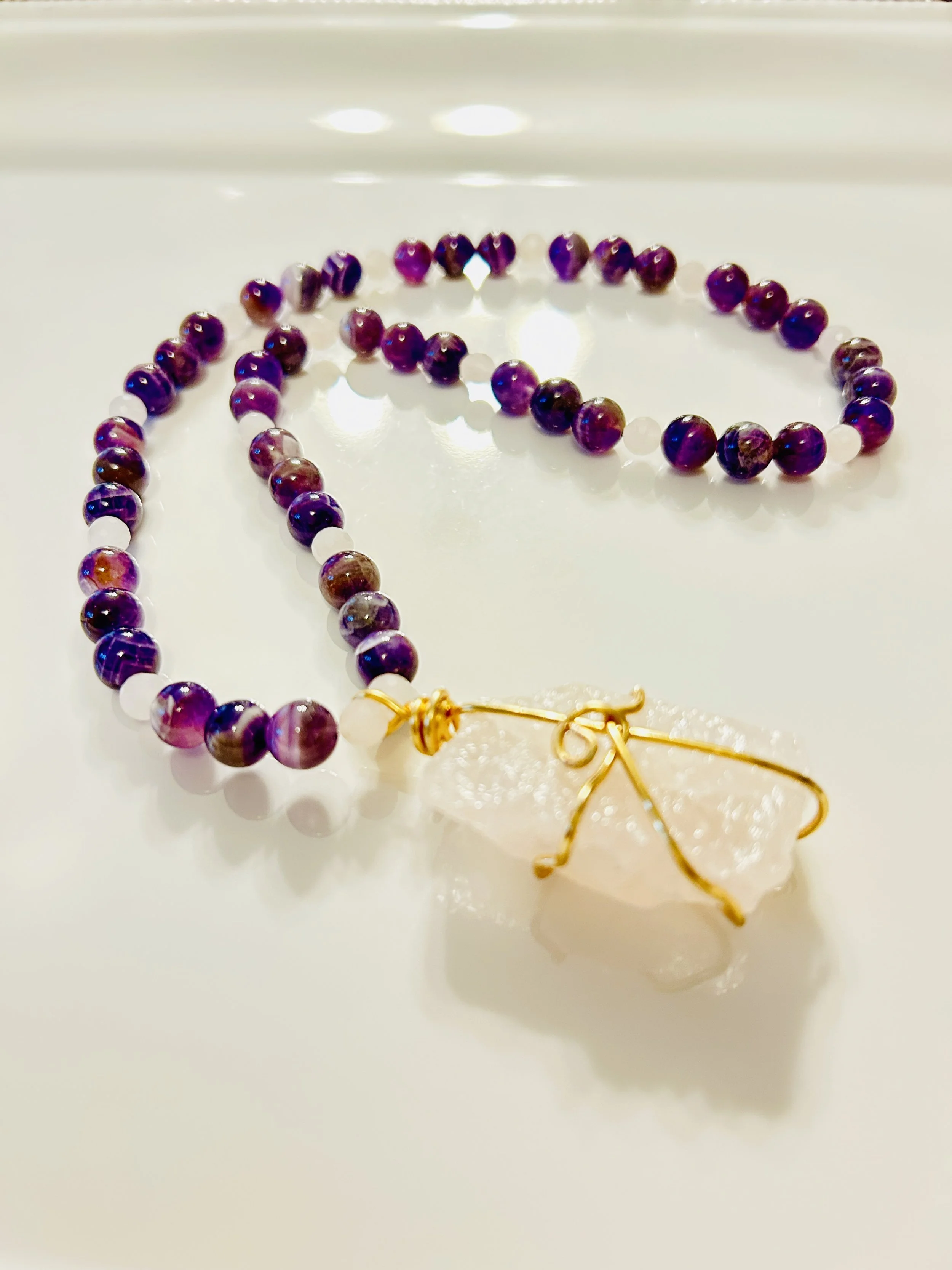 Beaded necklace with purple beads and a large white stone pendant wrapped with gold wire.