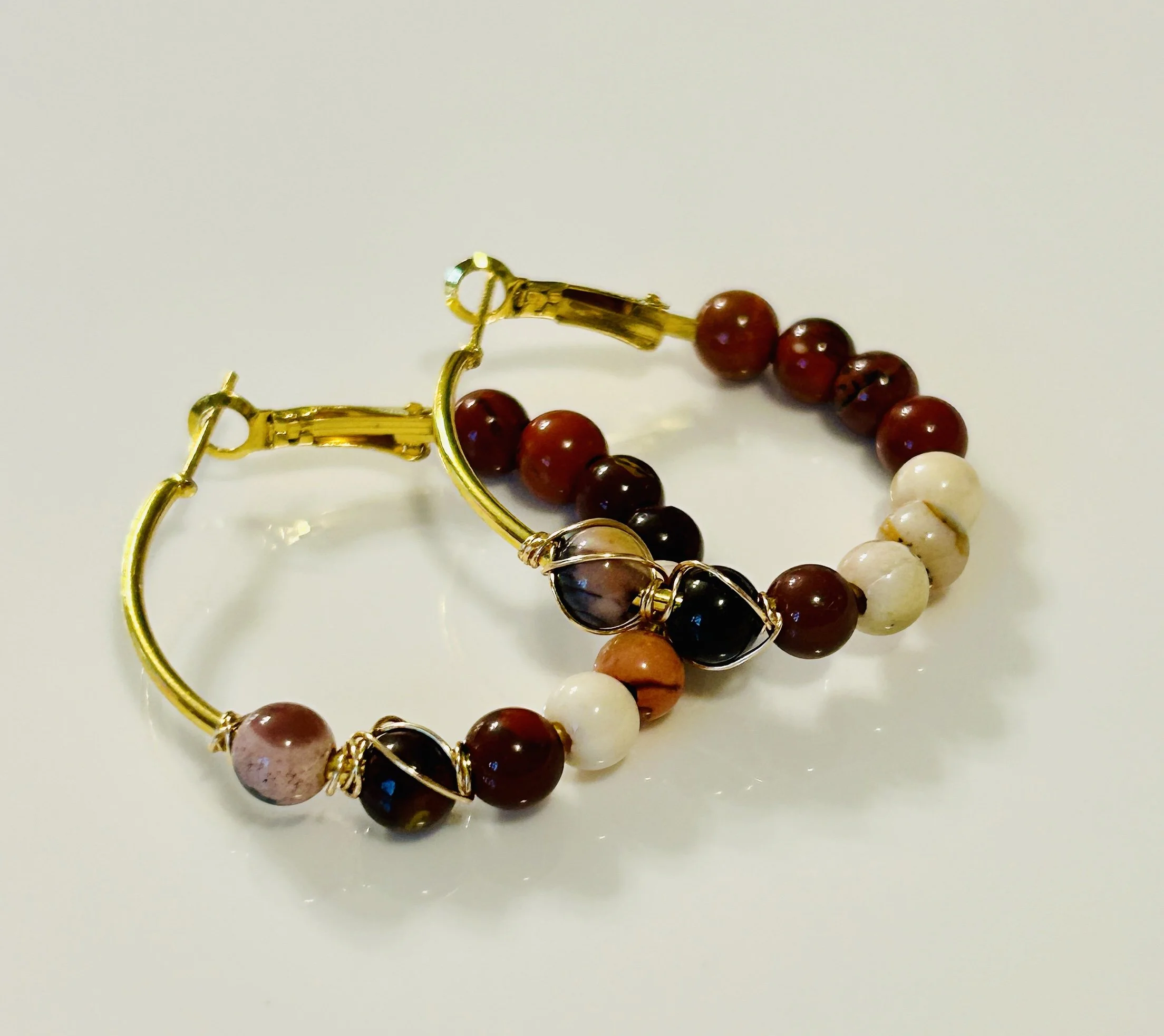 Gold hoop earrings with multi-colored beads, including brown, cream, and black beads, placed on a white surface.