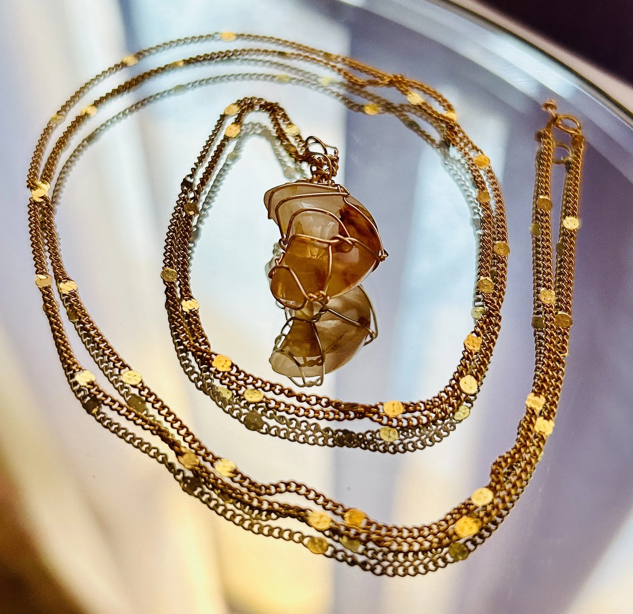 Multiple gold necklaces and a wire-wrapped bracelet with amber-colored stones on a reflective surface.