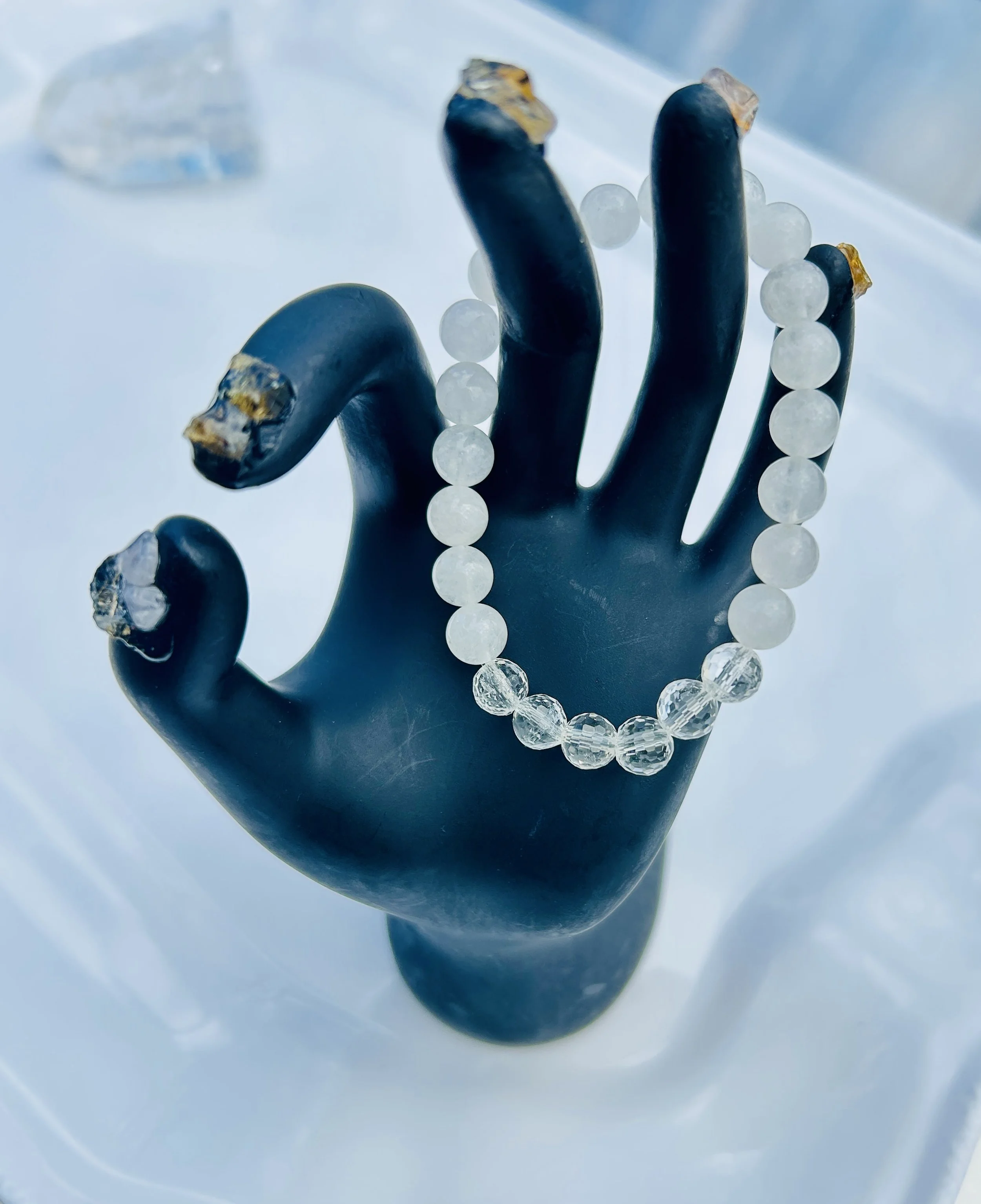 Black mannequin hand displaying a beaded bracelet made of white and clear round beads.