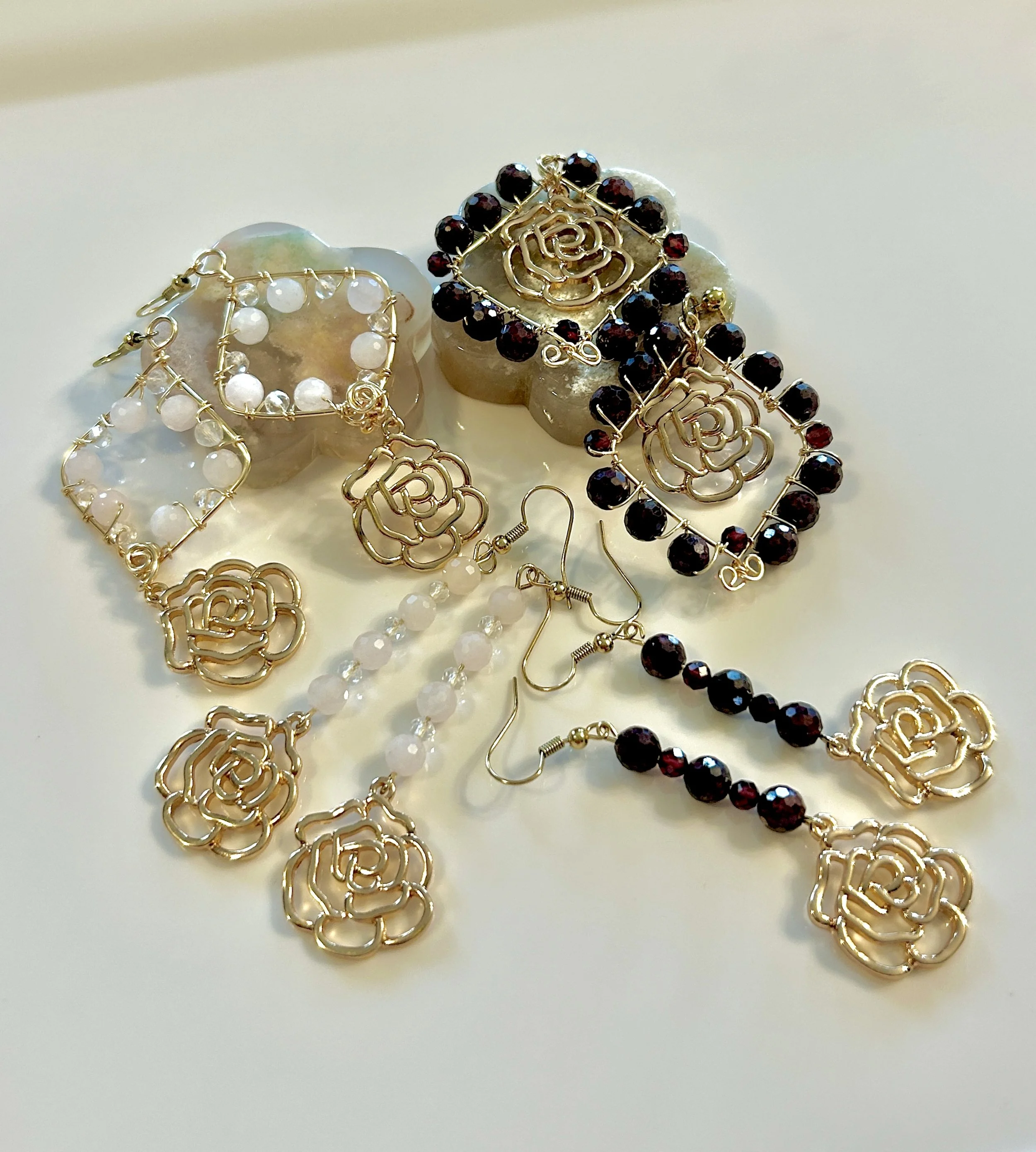 Gold floral jewelry set with earrings, necklaces, and rings, featuring white and dark red beads, arranged on a white surface.