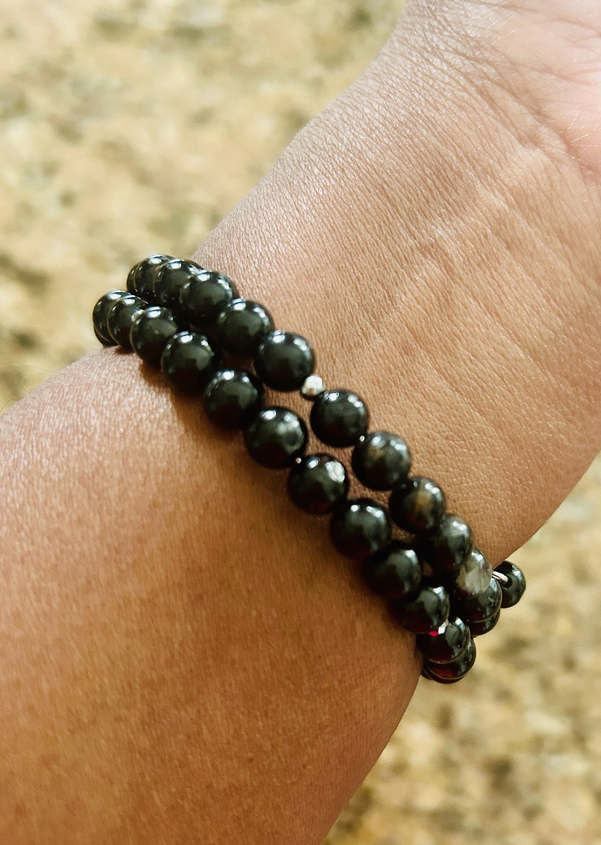 A person's wrist wearing a double-strand black beaded bracelet against a blurred outdoor background.