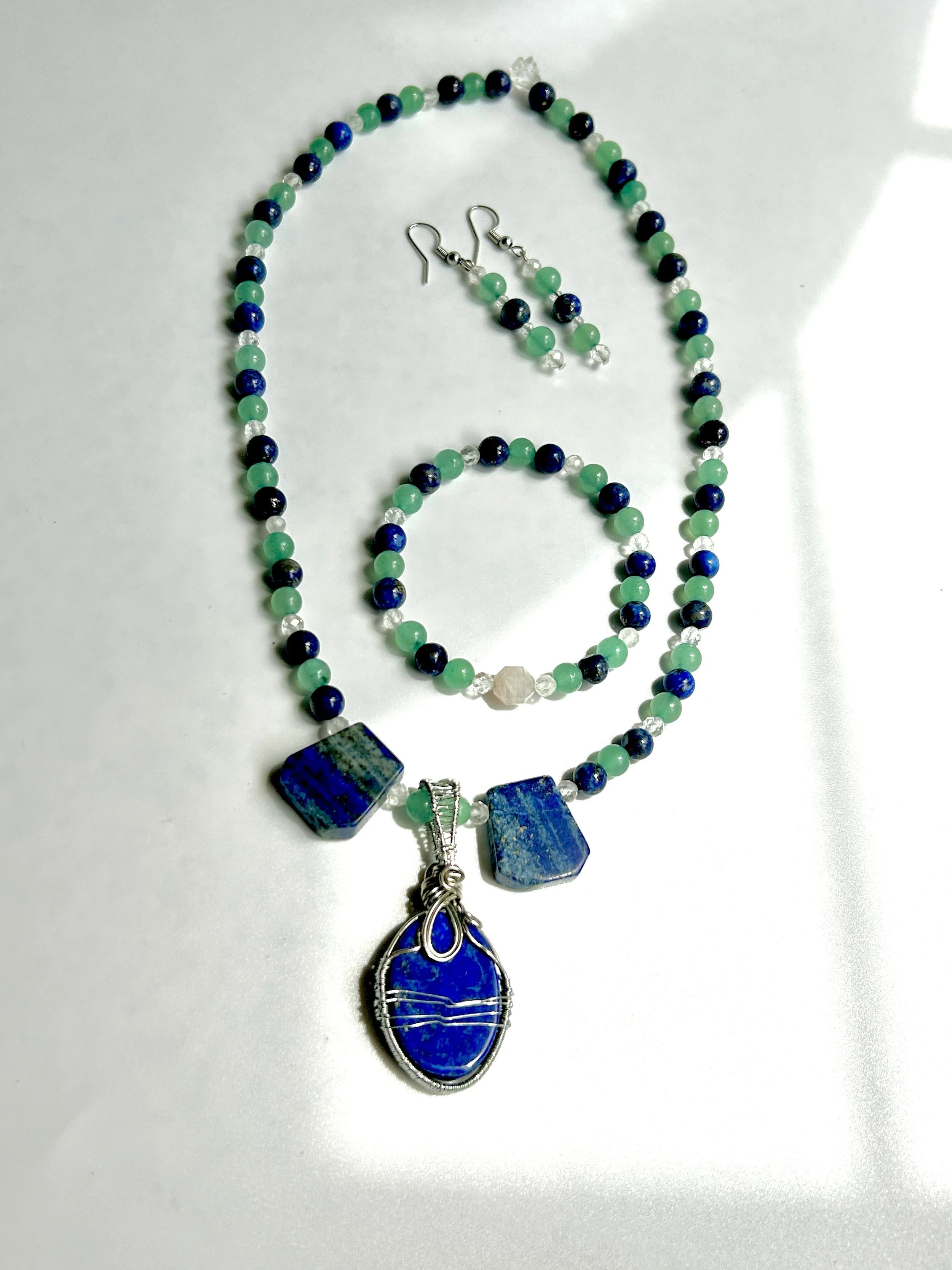Blue and green beaded jewelry set with a pendant necklace, matching earrings, a beaded bracelet, and a ring, all featuring blue gemstones.