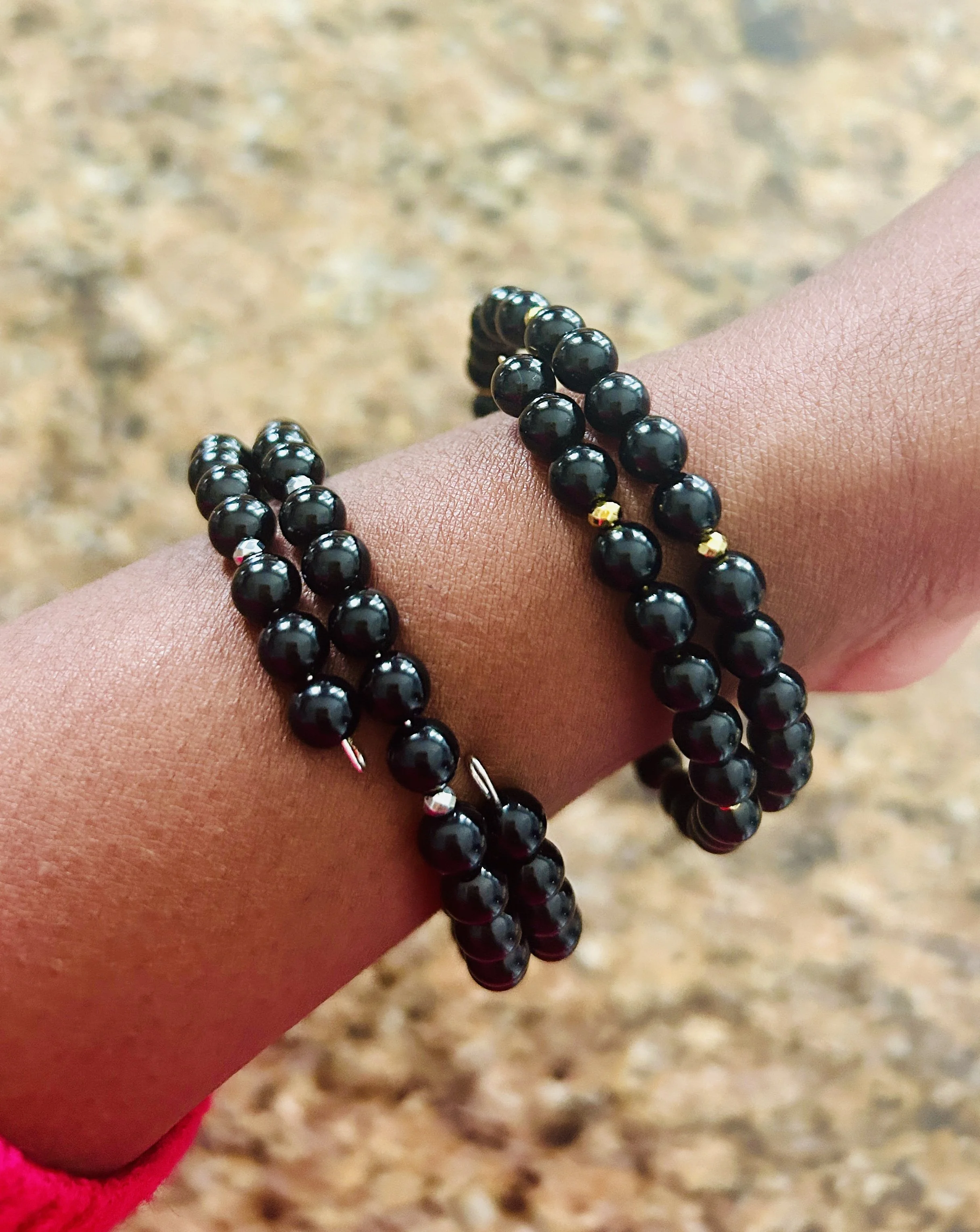 A hand with two black beaded bracelets with small gold and silver accents.