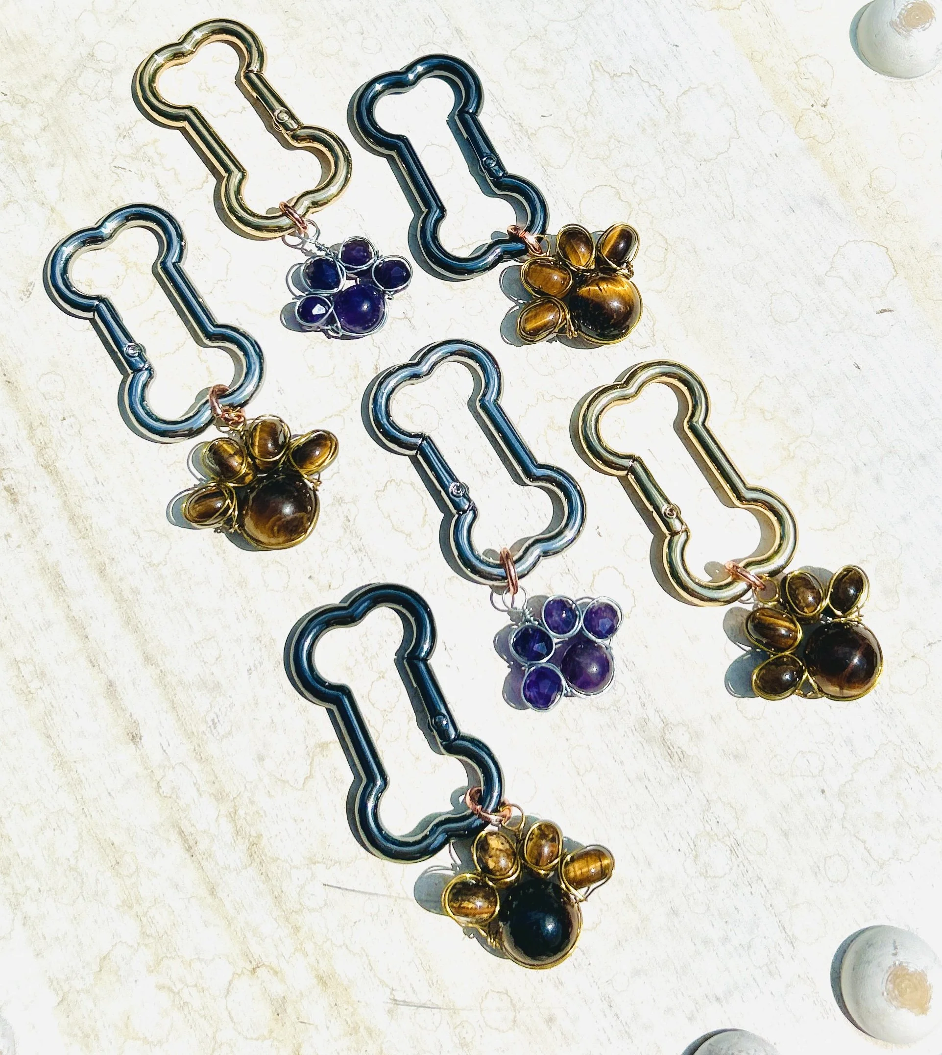 Five metal dog collar clips with decorative gemstone charms, three with purple stones and two with amber-colored stones, laid out on a light-colored surface.