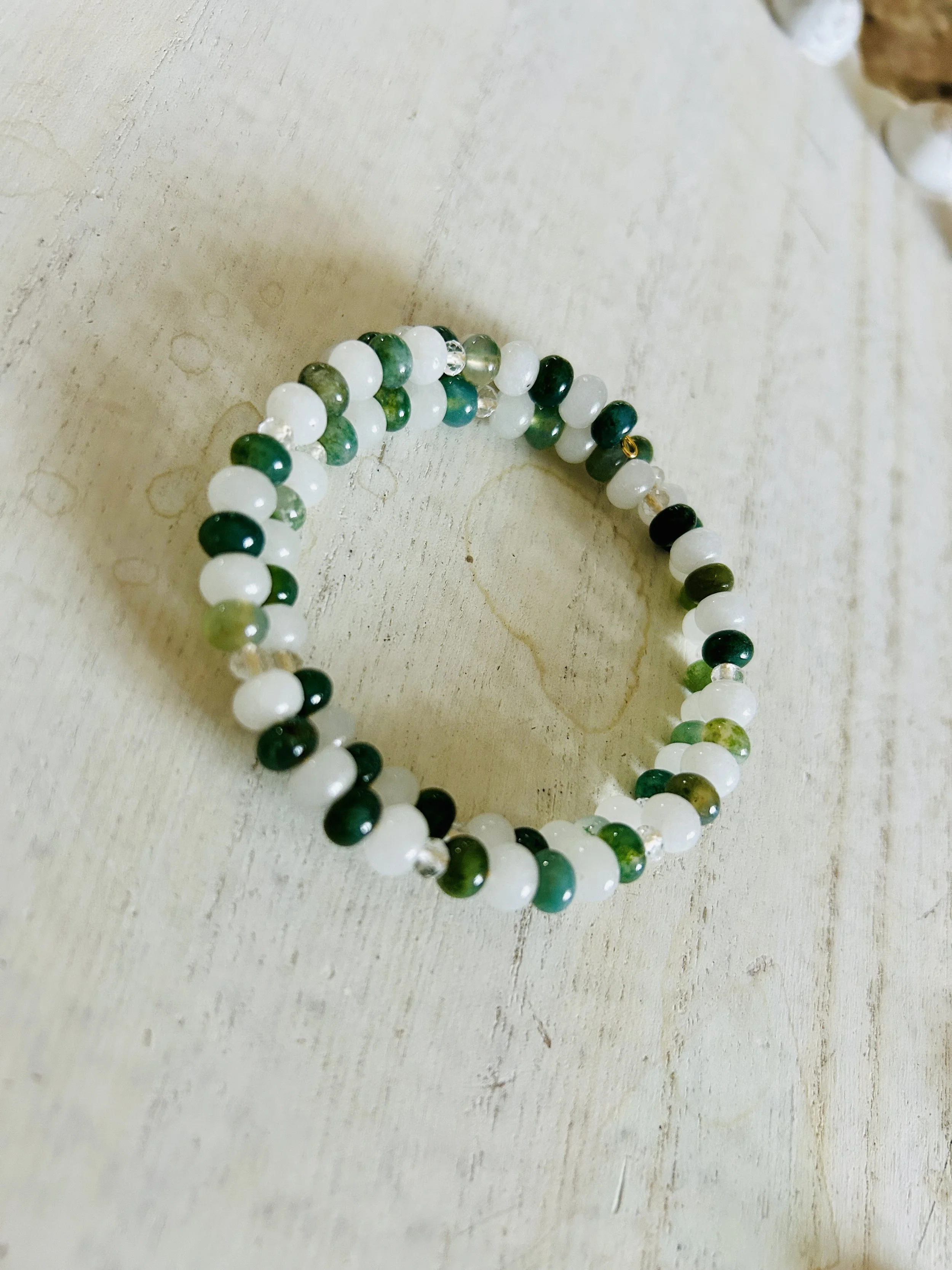 Beaded bracelet with white, green, and black beads, placed on a light-colored wooden surface.