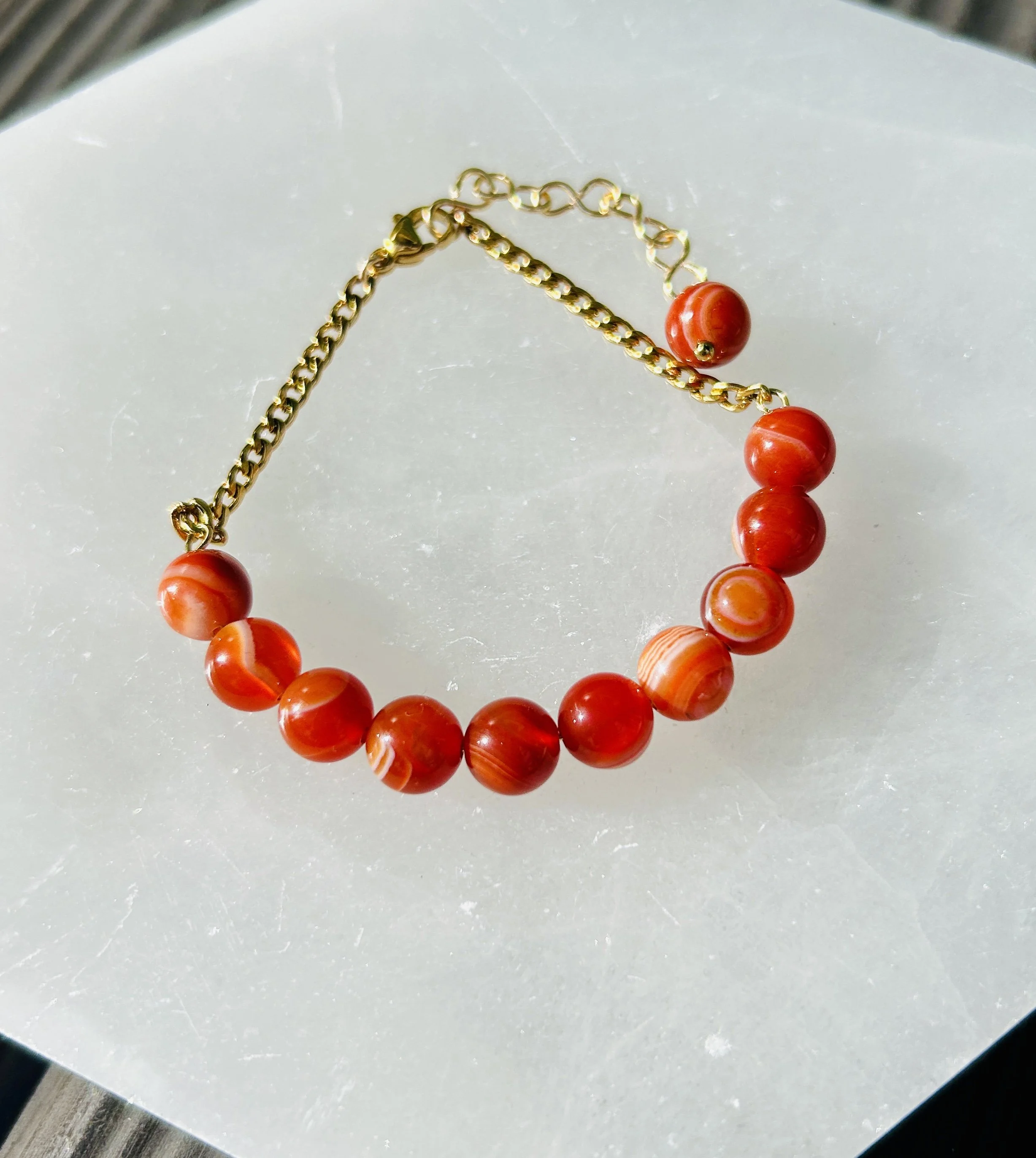Gold chain necklace with large orange beads laid on a white surface.