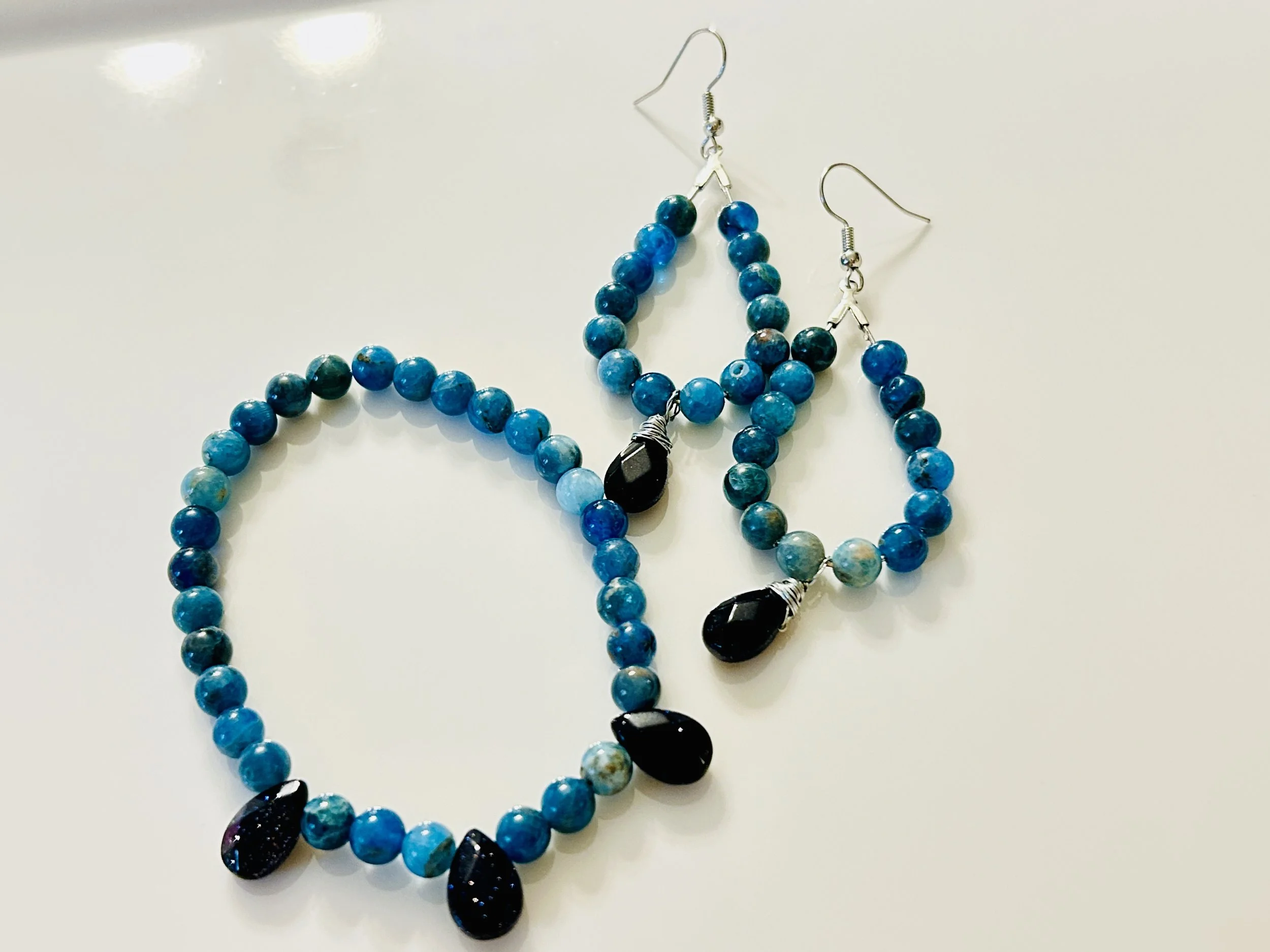 Blue beaded jewelry set with earrings and a necklace featuring black teardrop-shaped pendants.