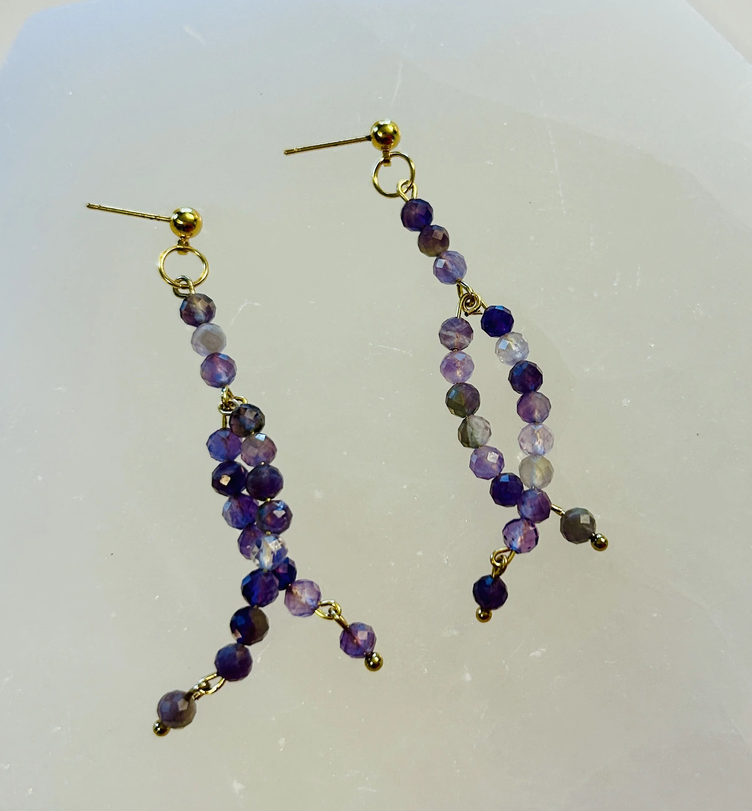 Gold and purple beaded dangling earrings on a plain background.