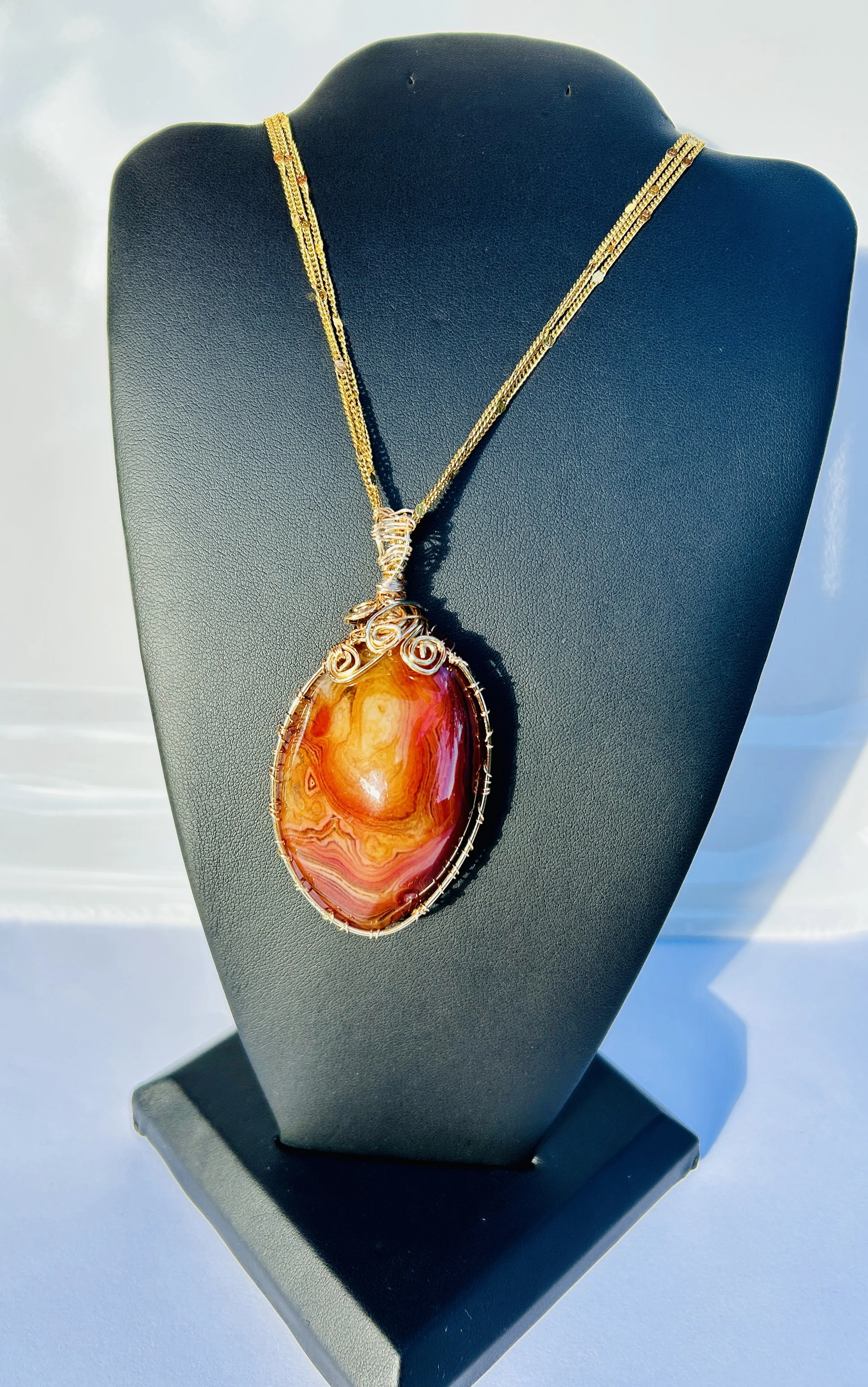 Gold necklace with large oval orange and red gemstone pendant on black display bust.