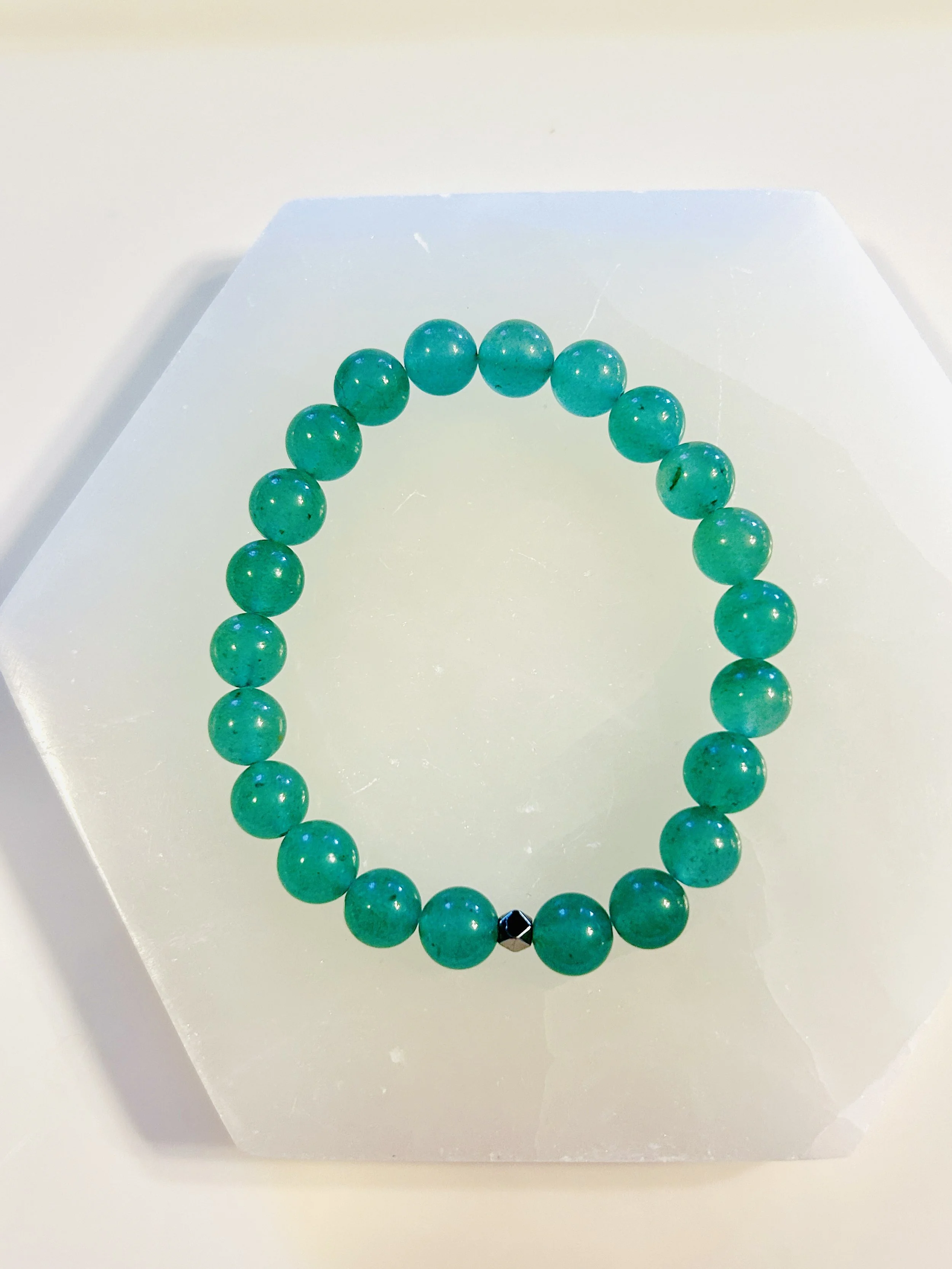 Green beaded bracelet with a single black bead, displayed on a white surface.