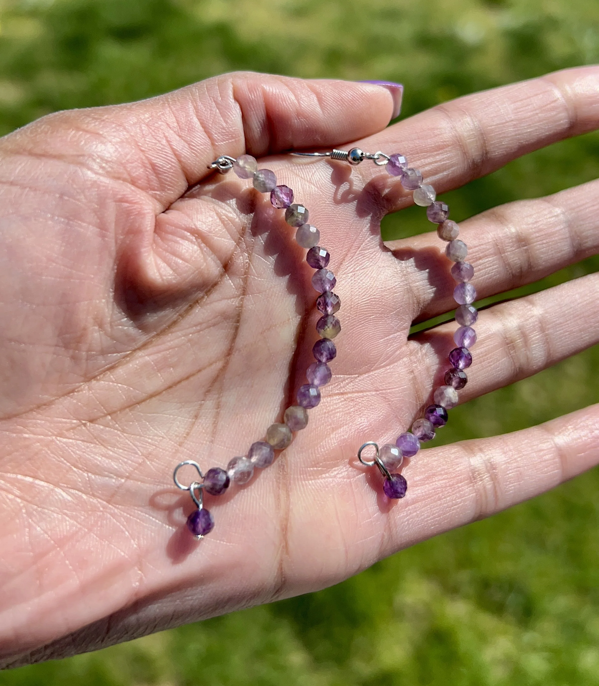 A hand holding a beaded purple gemstone necklace outdoors on grass.