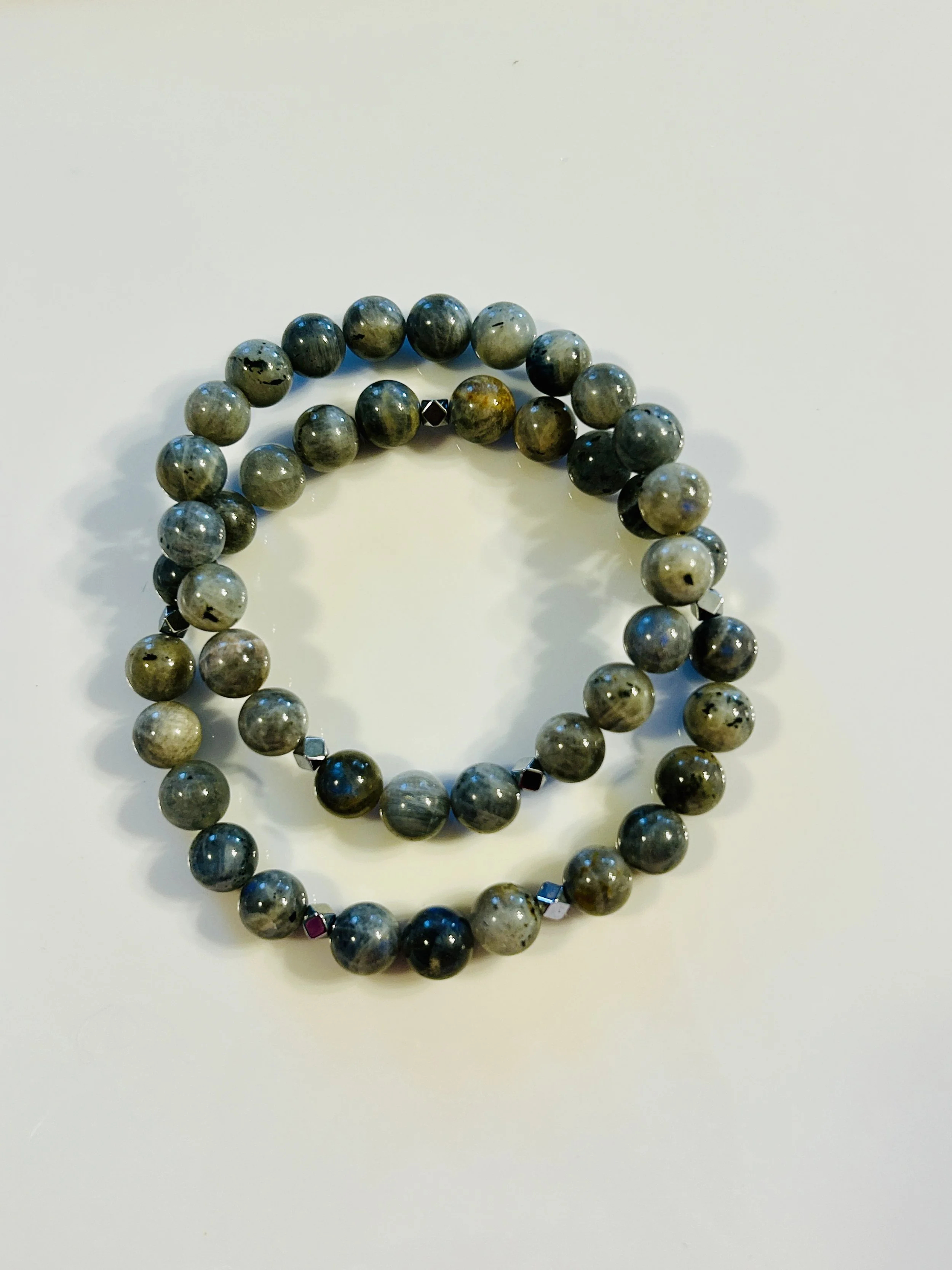 Two round beaded necklaces with black, gray, and metallic beads, arranged on a white surface.