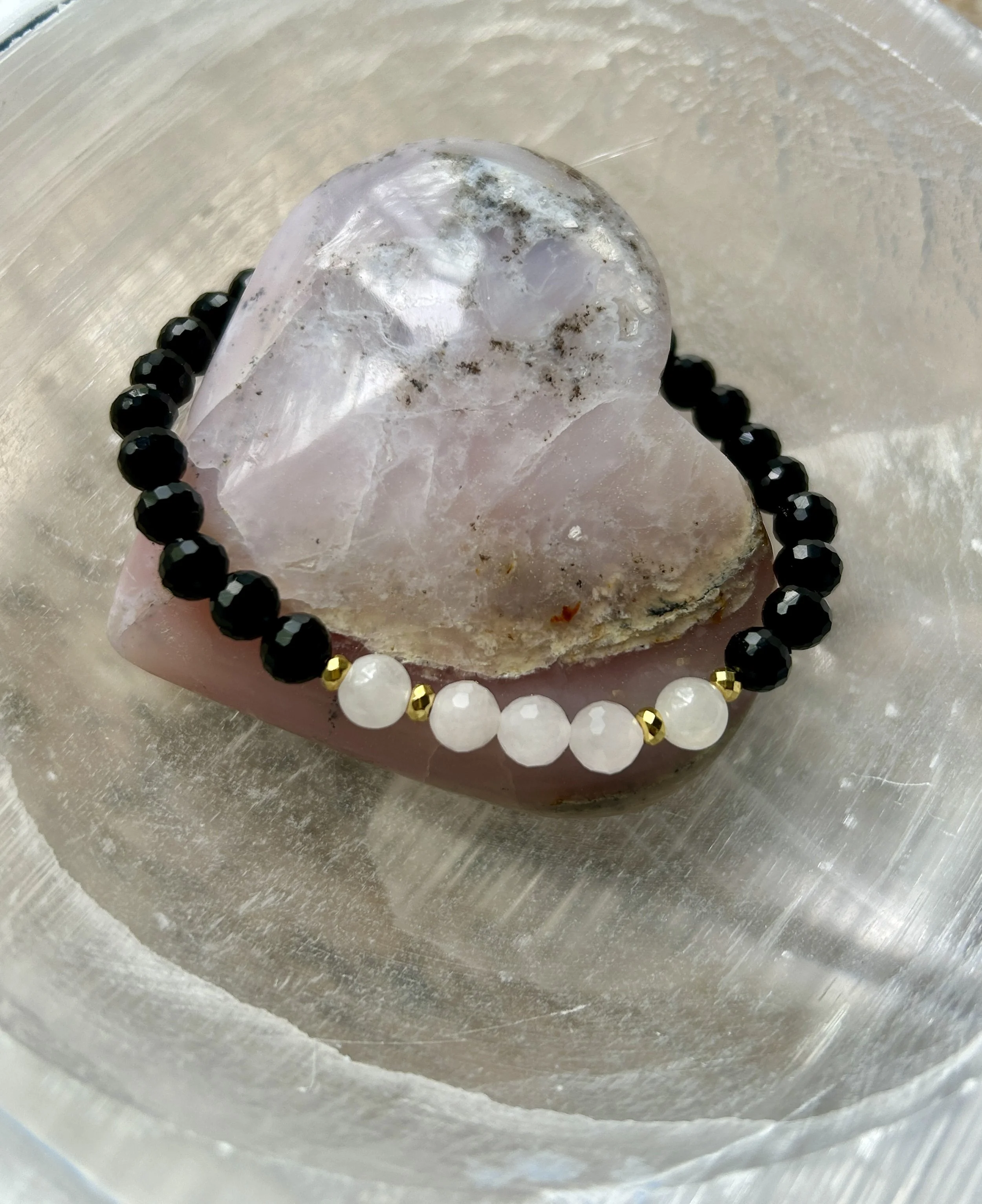 Black, white, and gold beaded bracelet resting on a pink and clear crystal heart.