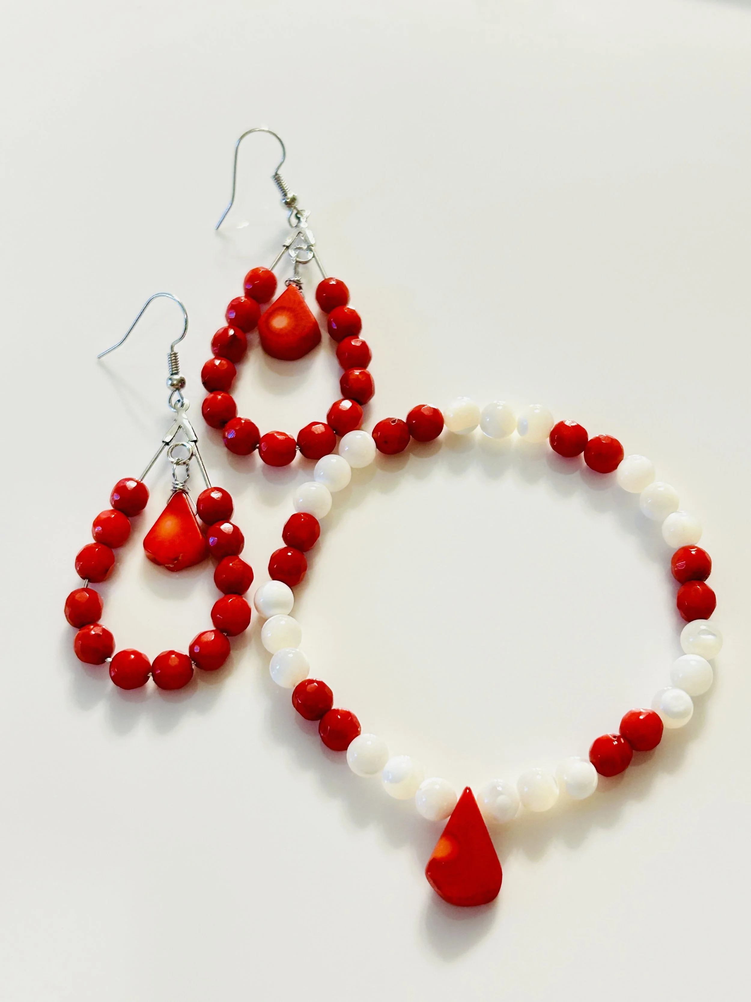 Red and white beaded jewelry set including earrings with teardrop and round beads, and a matching necklace with alternating red and white beads and a teardrop pendant.