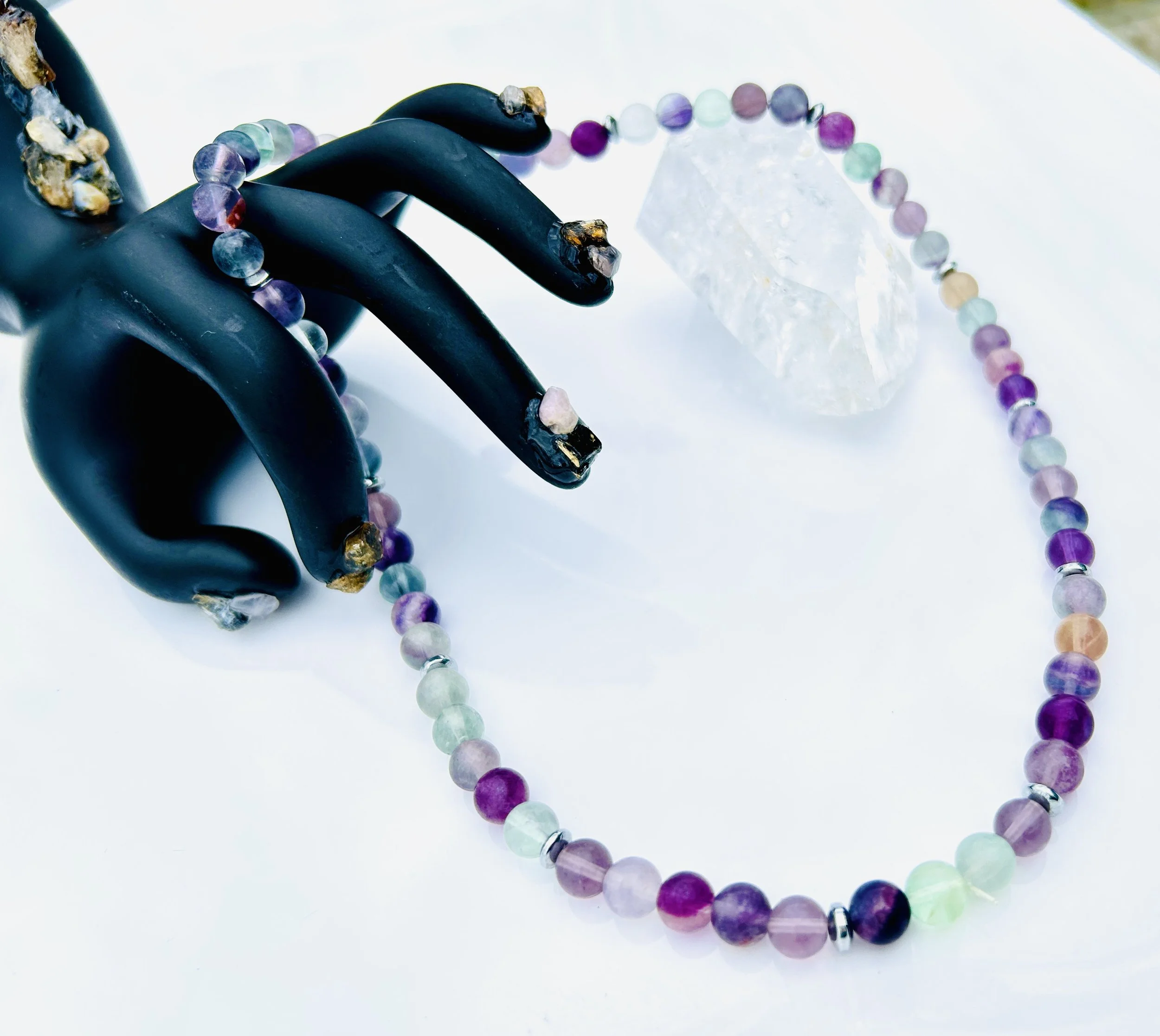 Colorful beaded necklace draped over a black jewelry display hand with a large clear crystal nearby on a white surface.