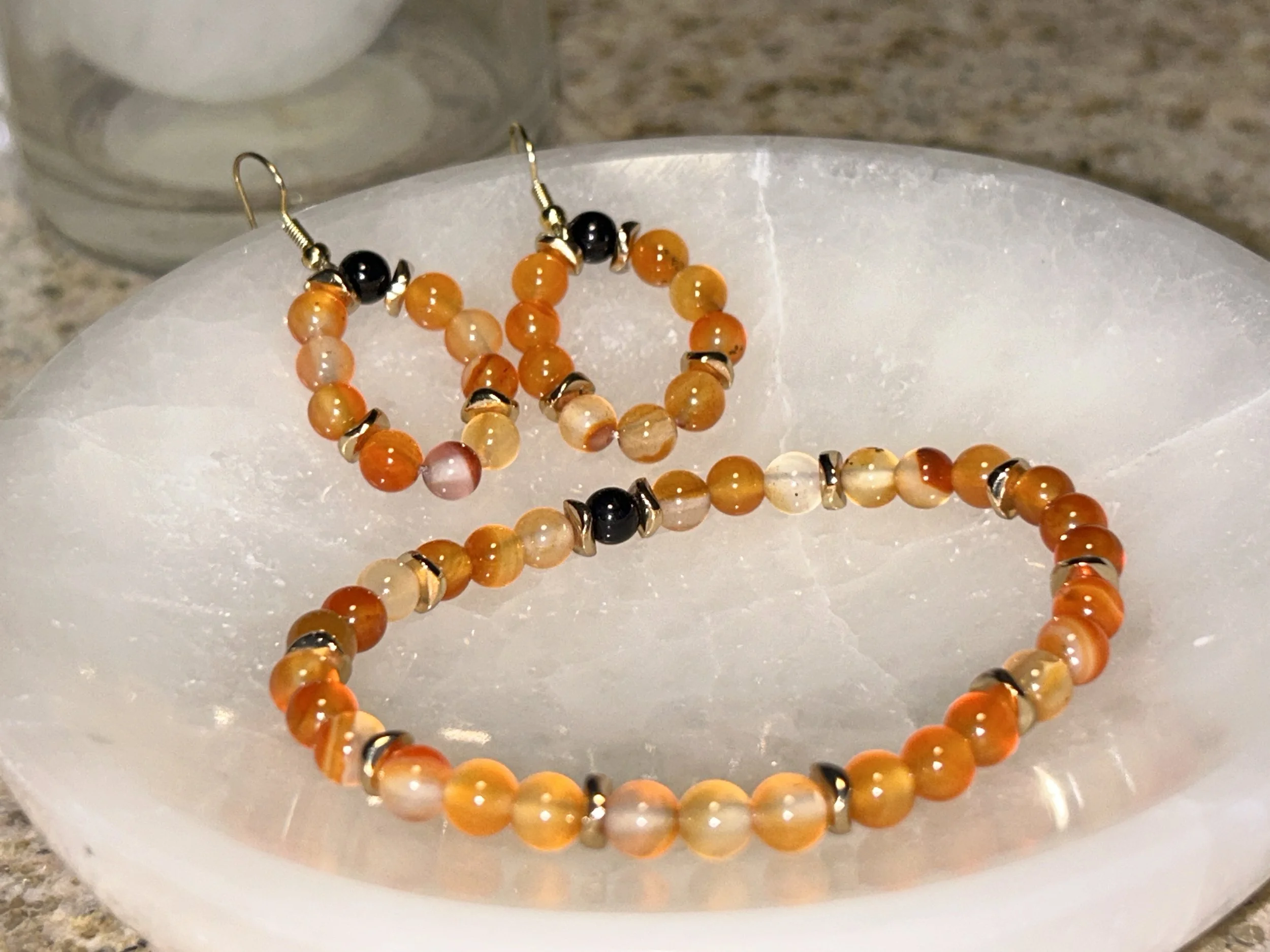 Orange, white, and black beaded jewelry bracelet and earrings with metal accents, resting on a white shell.