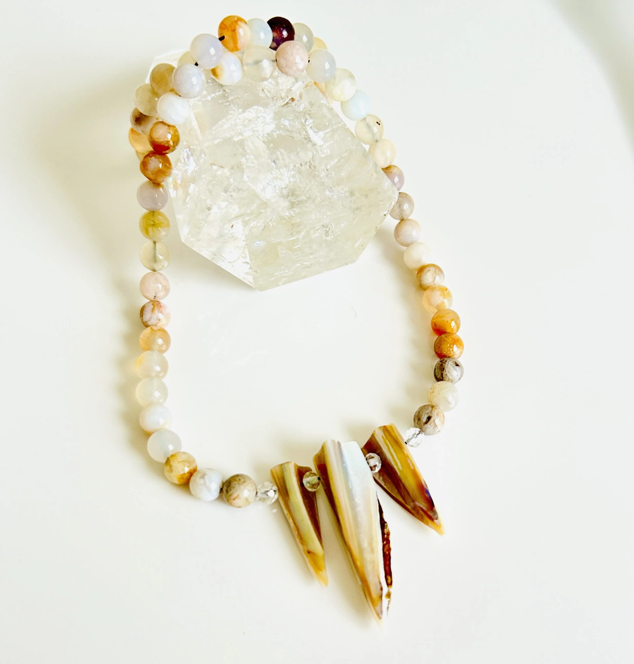 A beaded necklace with three large shell pendants and a clear quartz crystal on a white surface.