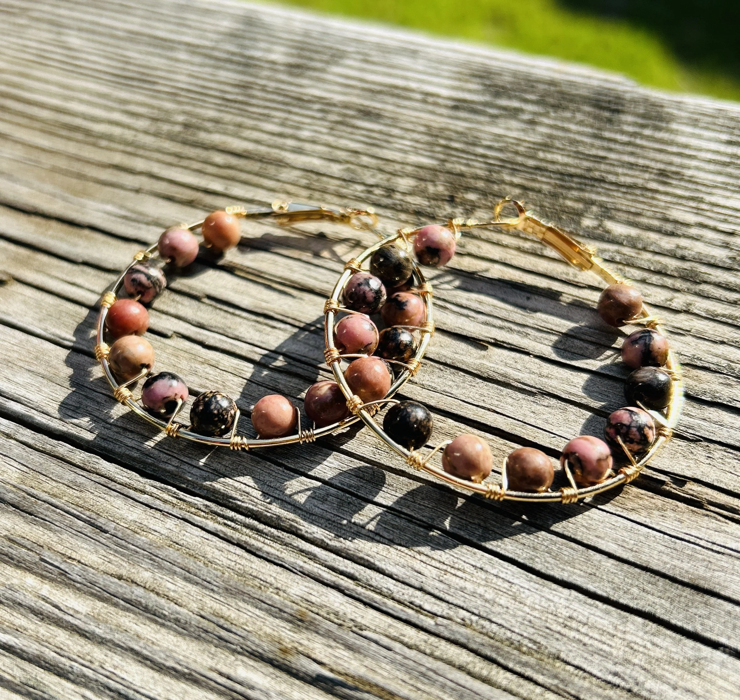 Gold wire hoop earrings with round pink and black marbled beads, resting on weathered wooden surface.