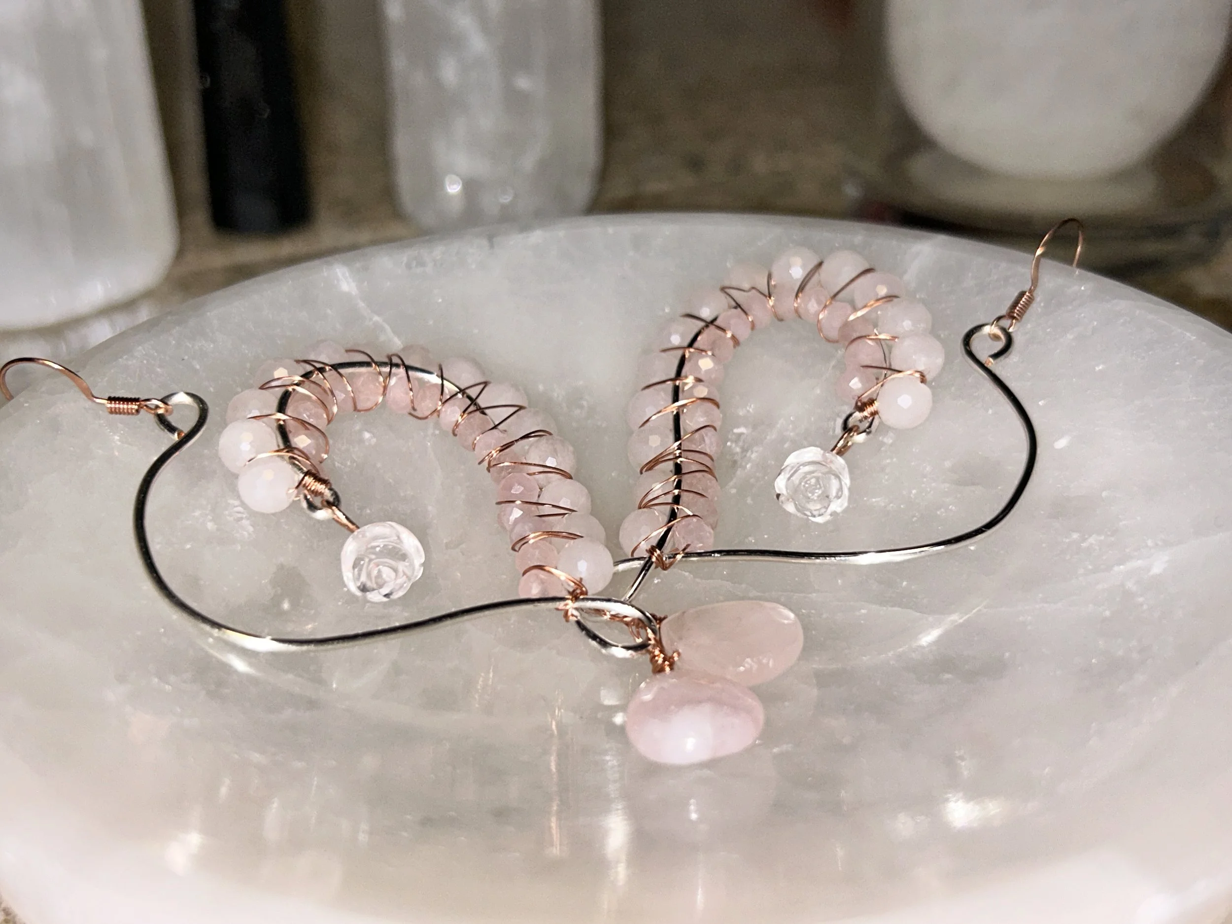 A pair of pink beaded earrings with clear and pink stones, placed on a white marble surface.