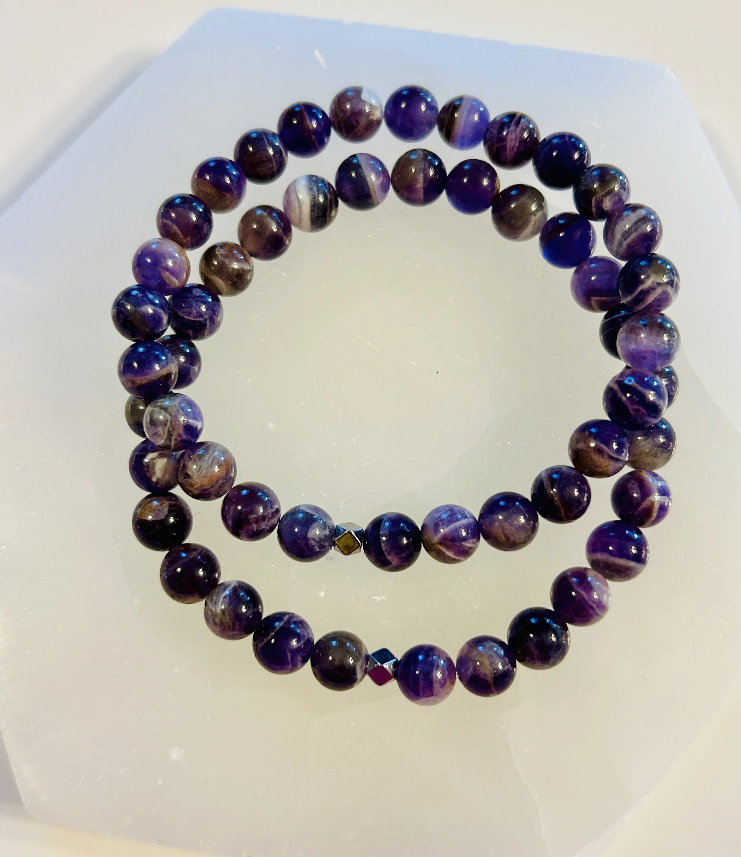 A purple beaded necklace with round beads, arranged in a circle on a white surface.