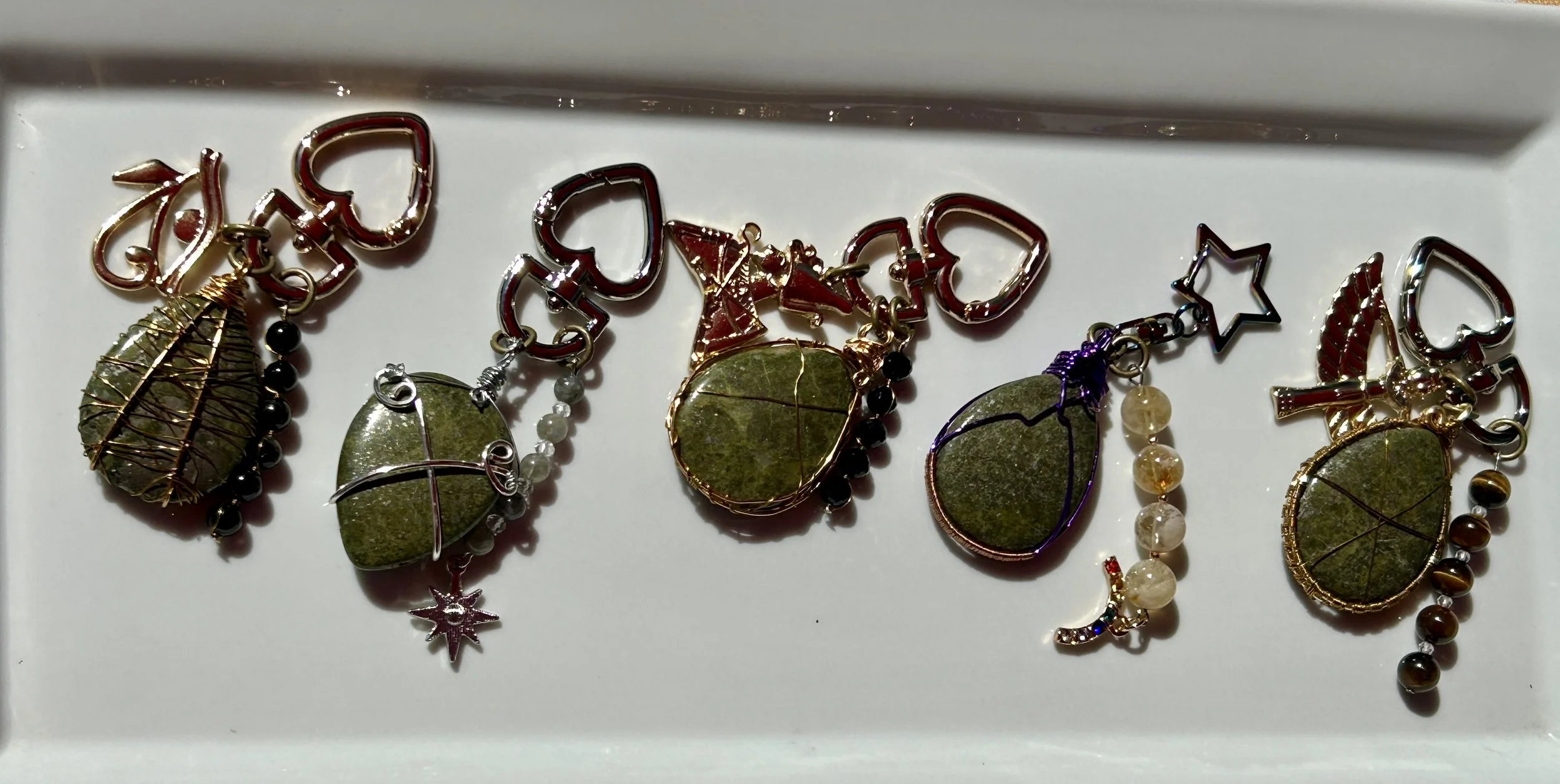 Collection of five earrings with green leaf pendants, each with unique wire and bead designs, arranged on a white surface.
