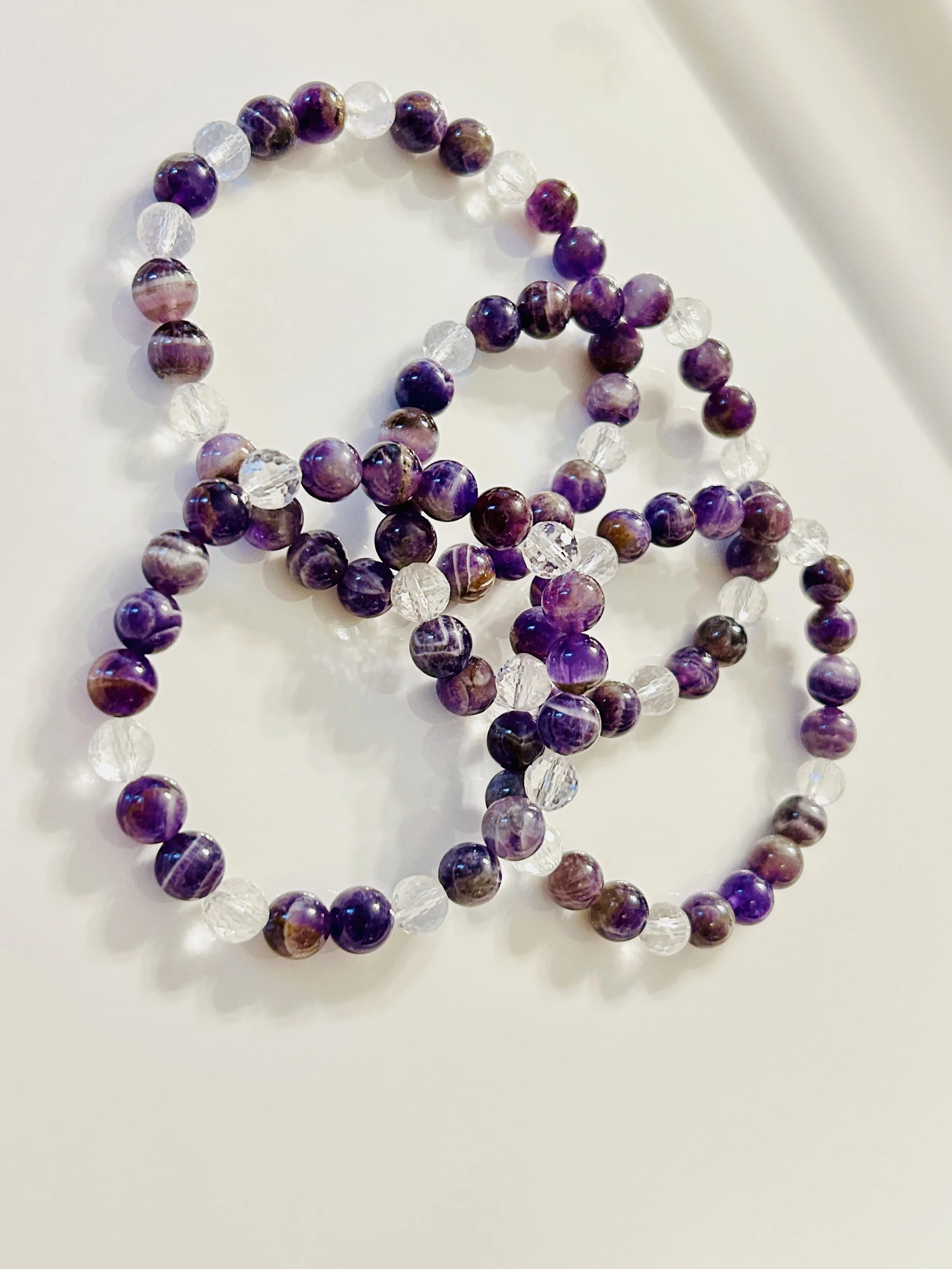 Three beaded necklaces made of purple and clear beads on a white surface.