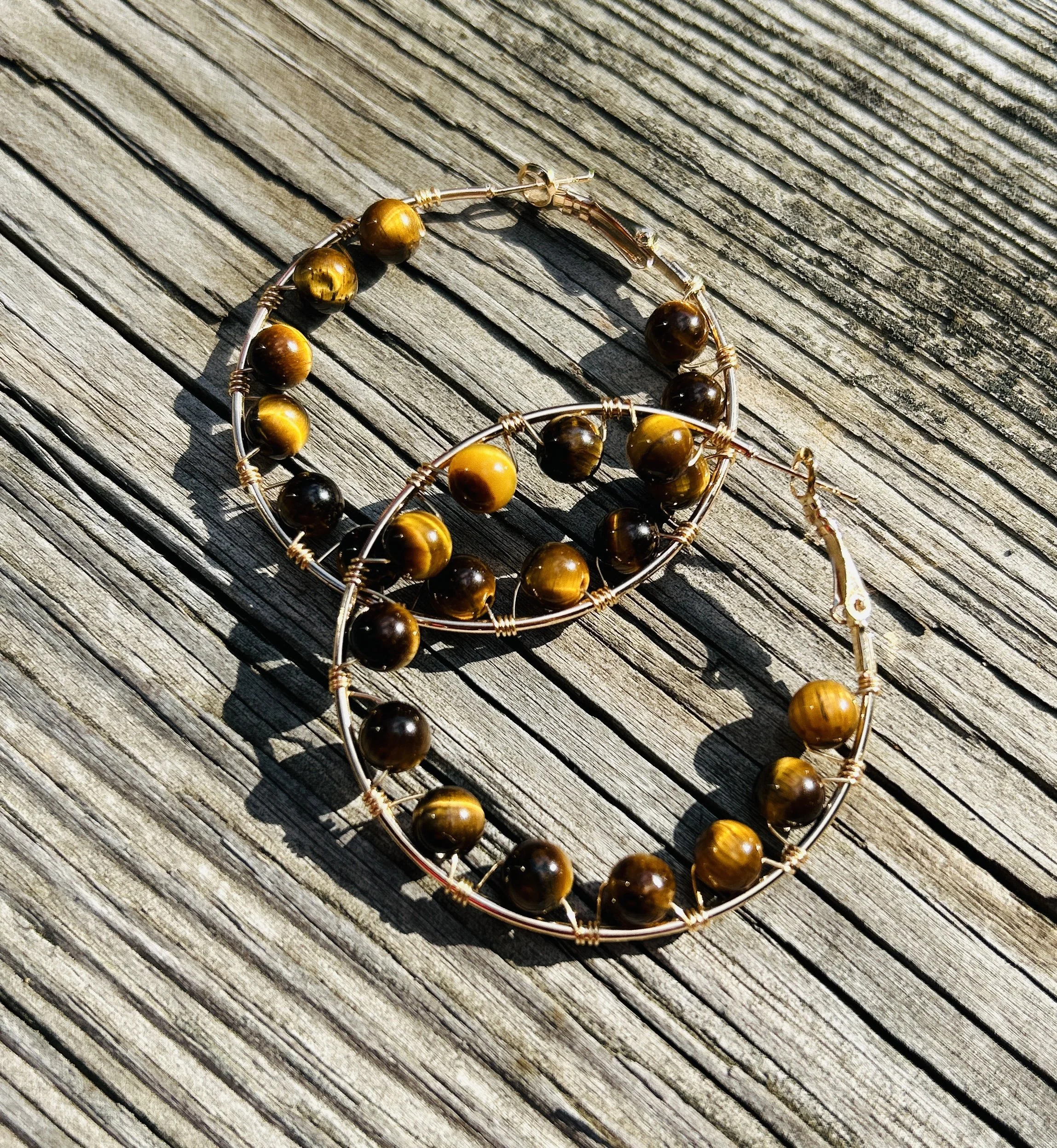 Two wire hoop earrings with yellow and dark brown beads, lying on weathered wooden surface.