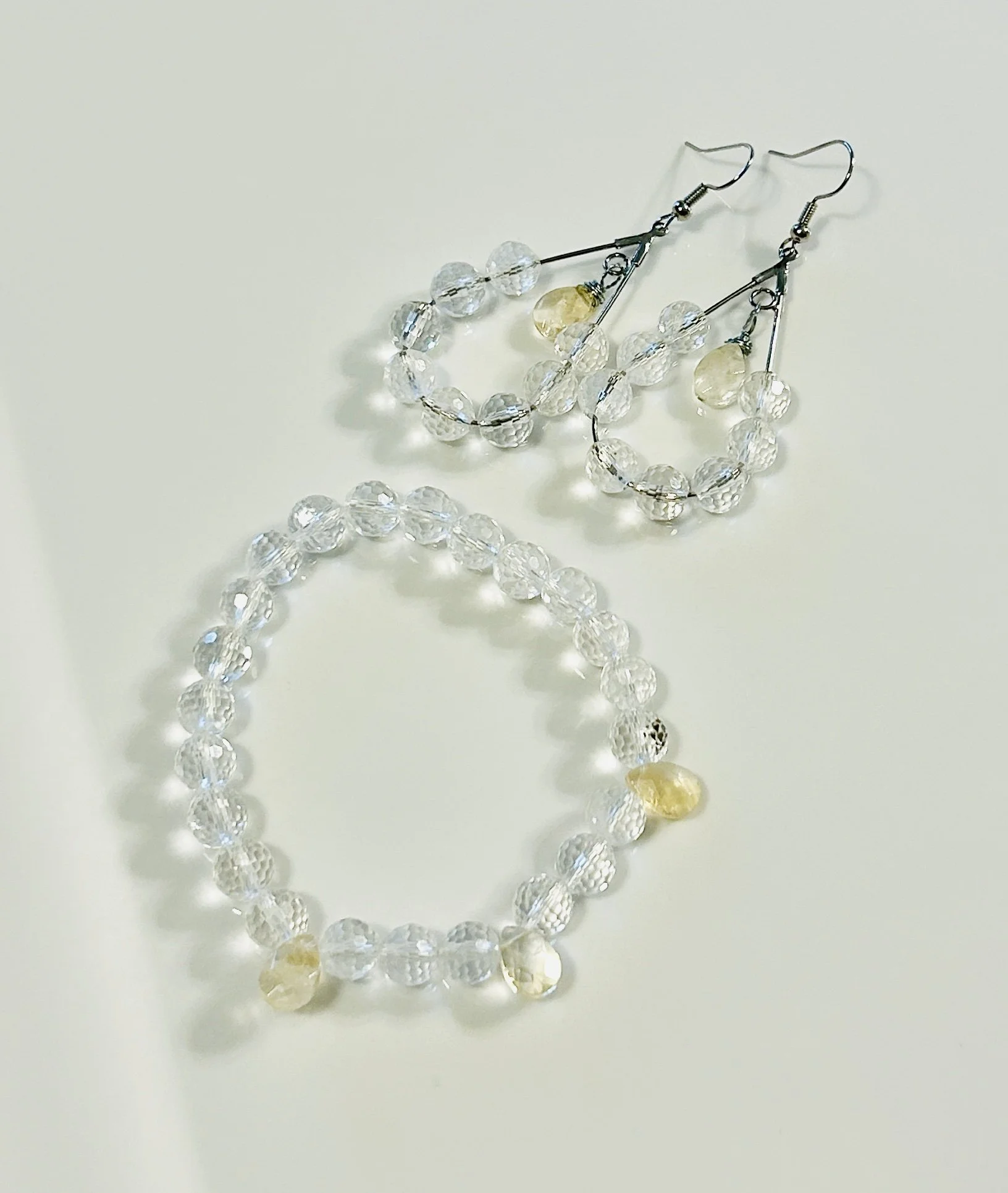Pair of clear beaded hoop earrings and a matching beaded bracelet with yellow beads, all on a white background.