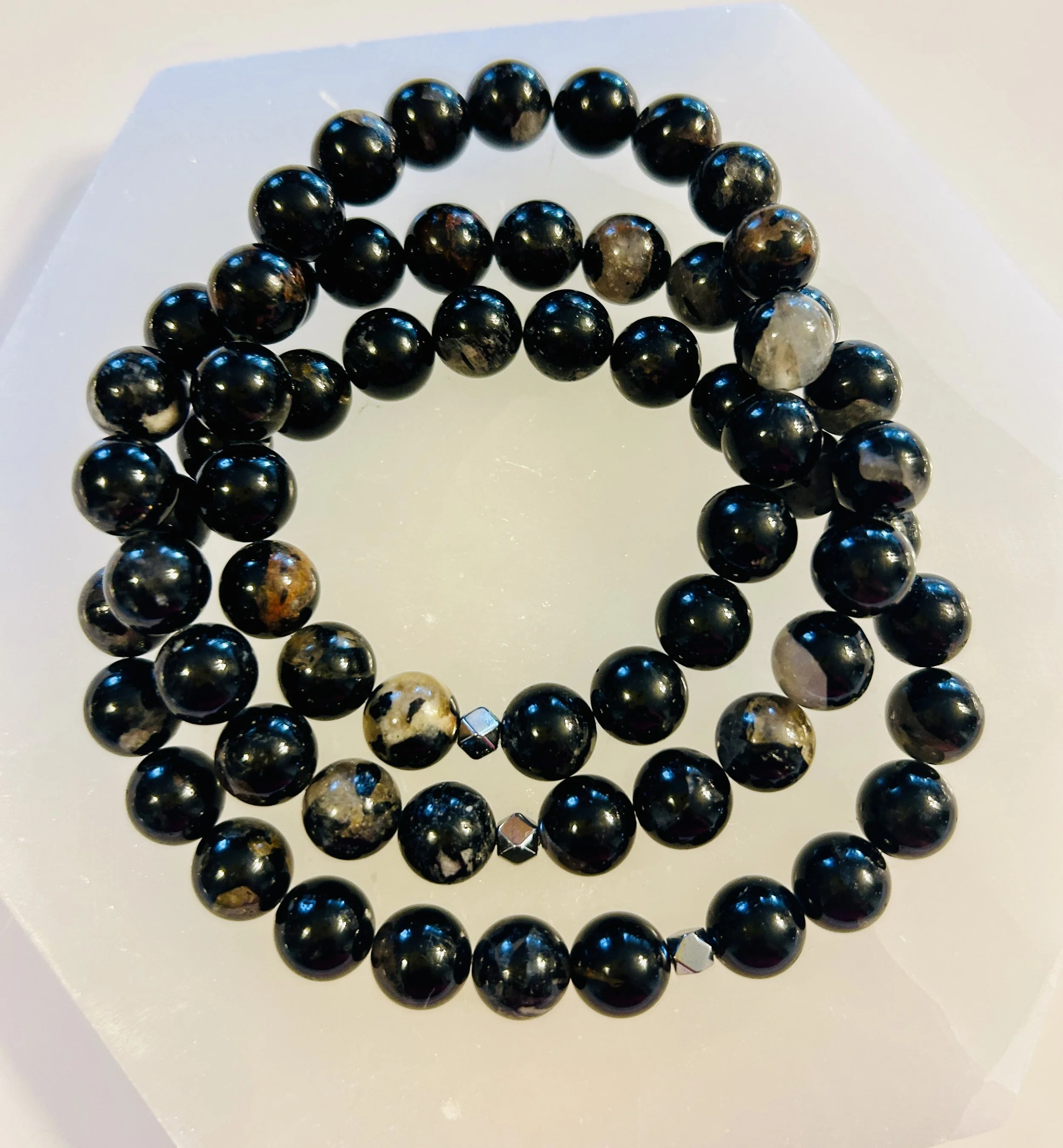 Black beaded bracelet with some beads showing gray and tan marbled patterns, placed on a white surface.