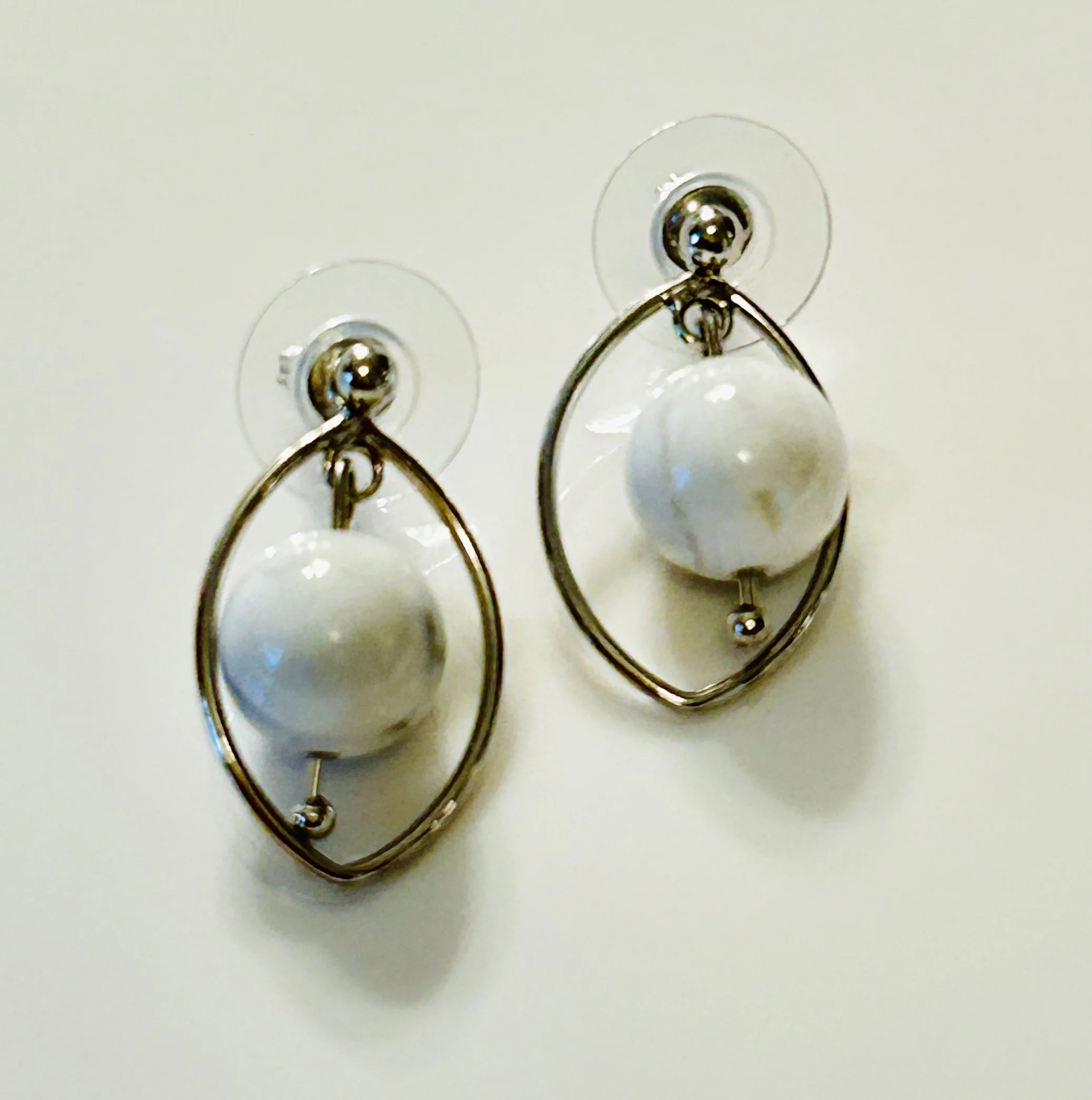 A pair of earrings with large white pearls and silver geometric frames hanging on a white background.