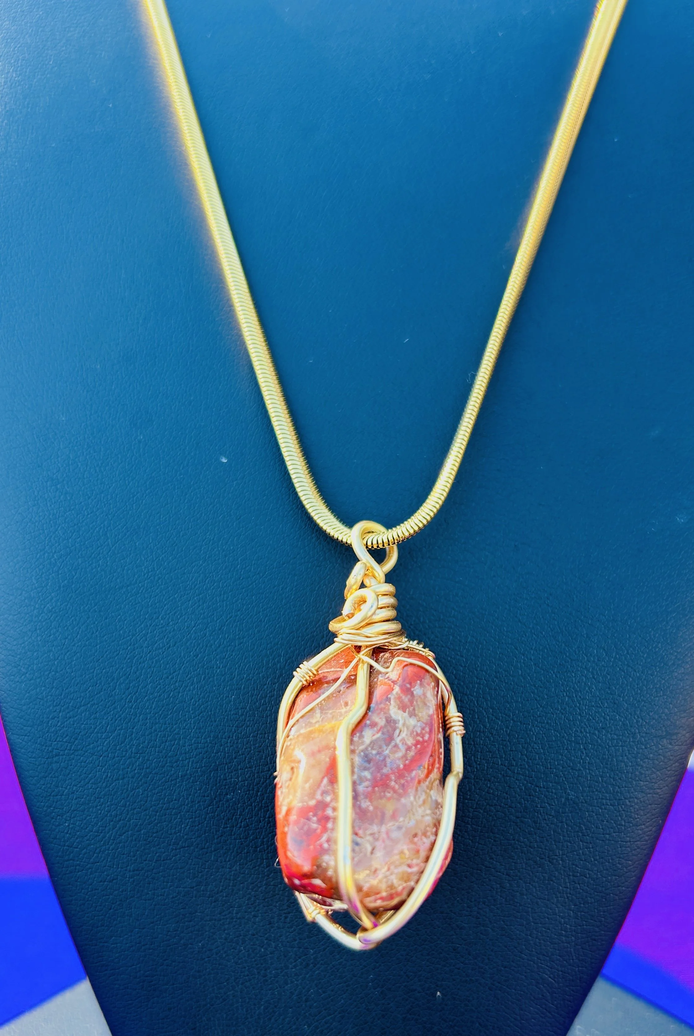 Gold necklace with a large, irregularly shaped pink and orange stone pendant wrapped in gold wire.