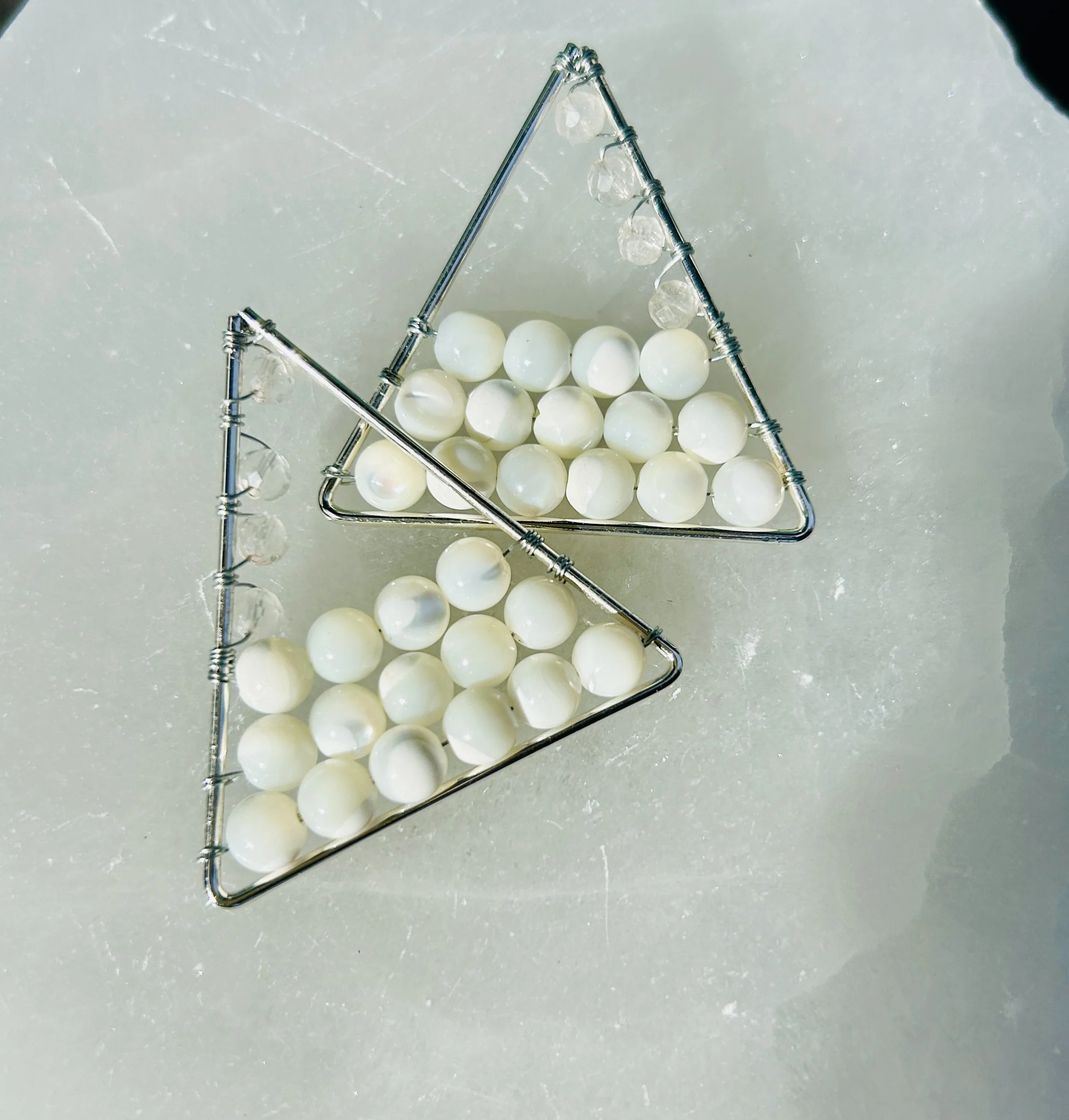 Two triangle-shaped metal frames filled with white pearls, placed on a light-colored surface.