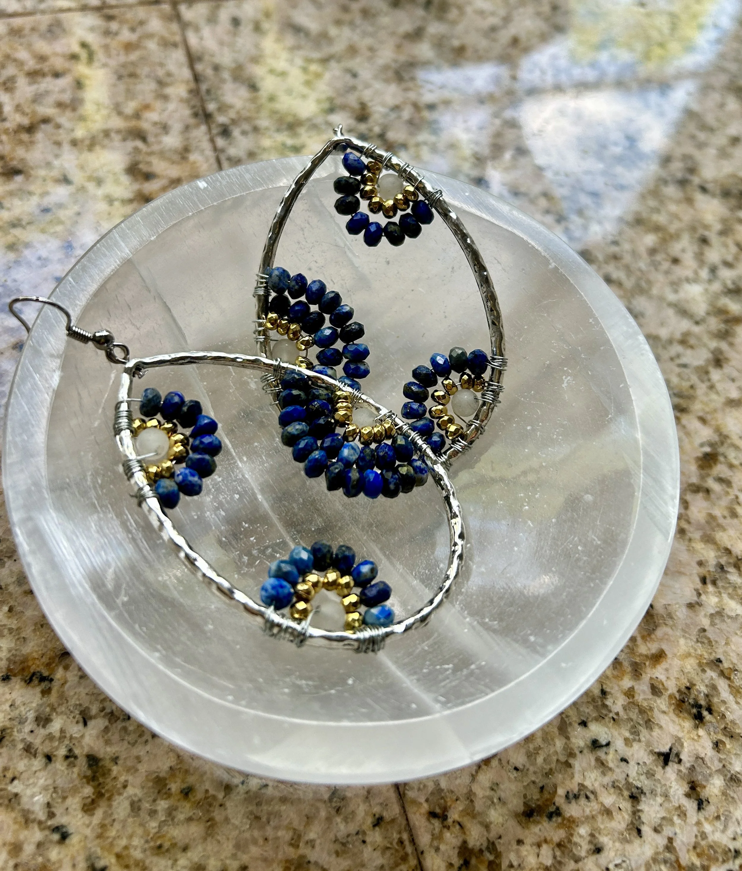 Silver jewelry set with blue and gold beads, including earrings and a necklace, displayed on a white dish on a granite countertop.