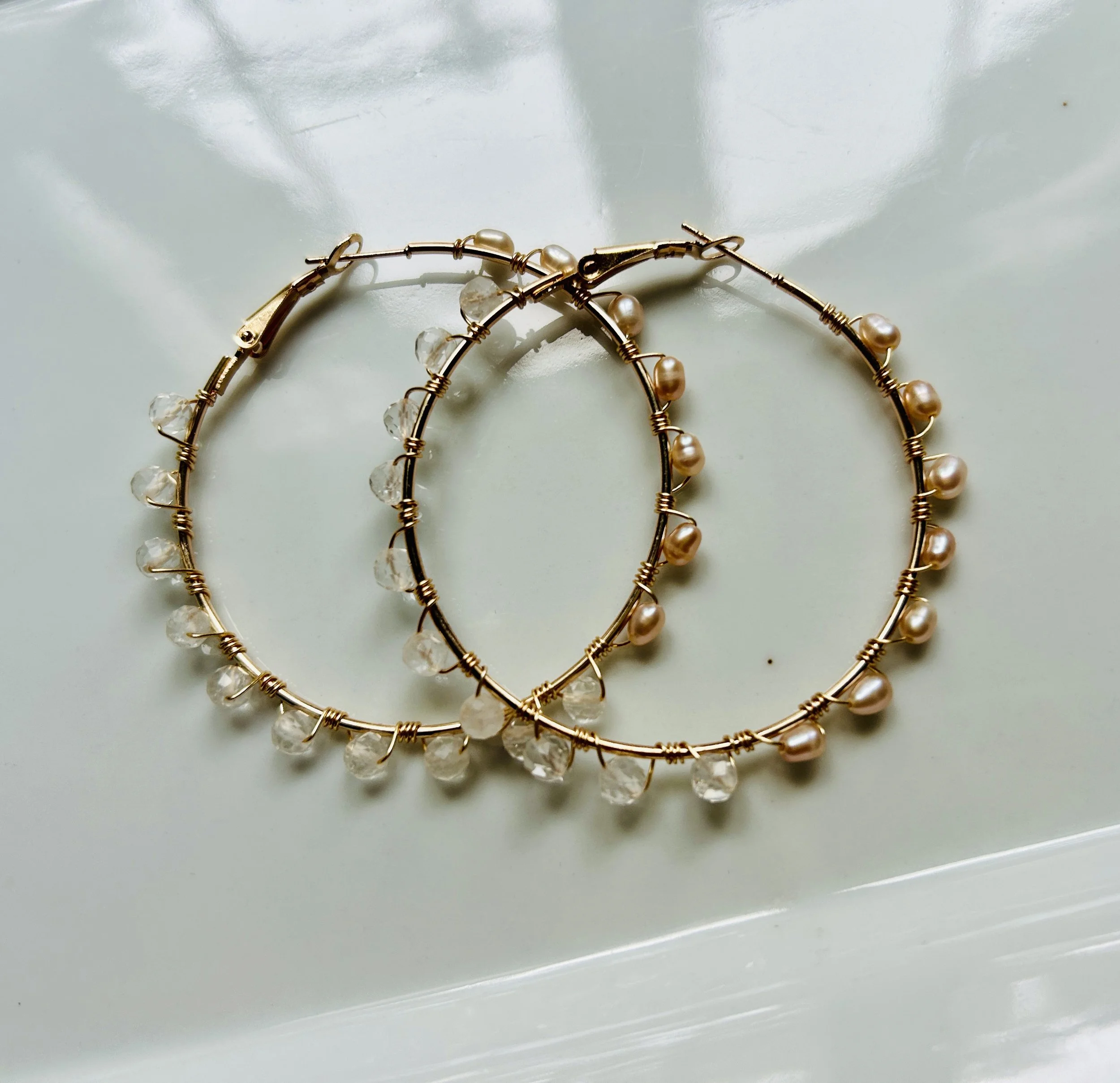 A set of three gold hoop earrings with different pearl and crystal bead embellishments, arranged on a shiny white surface.