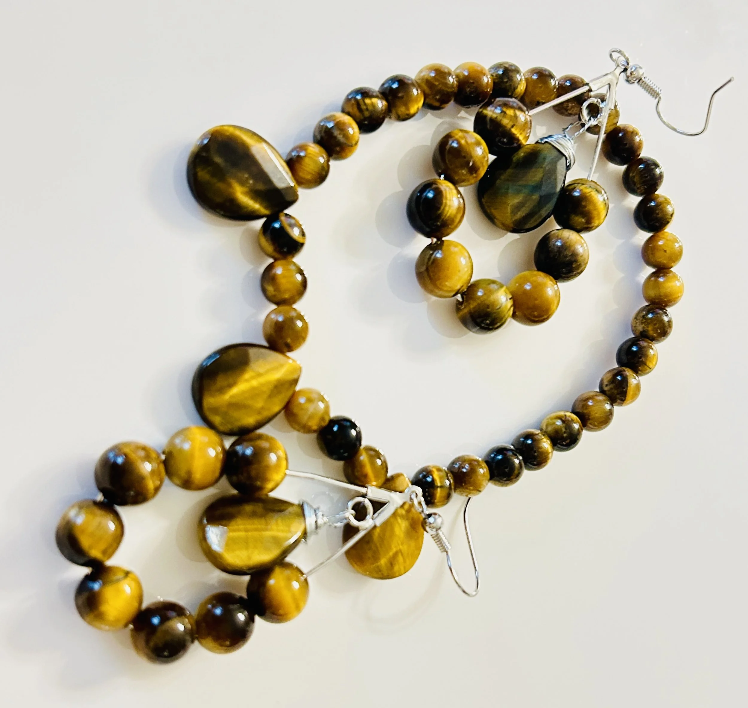 Set of tiger's eye jewelry including a necklace and earrings with round and teardrop-shaped beads on a white background.