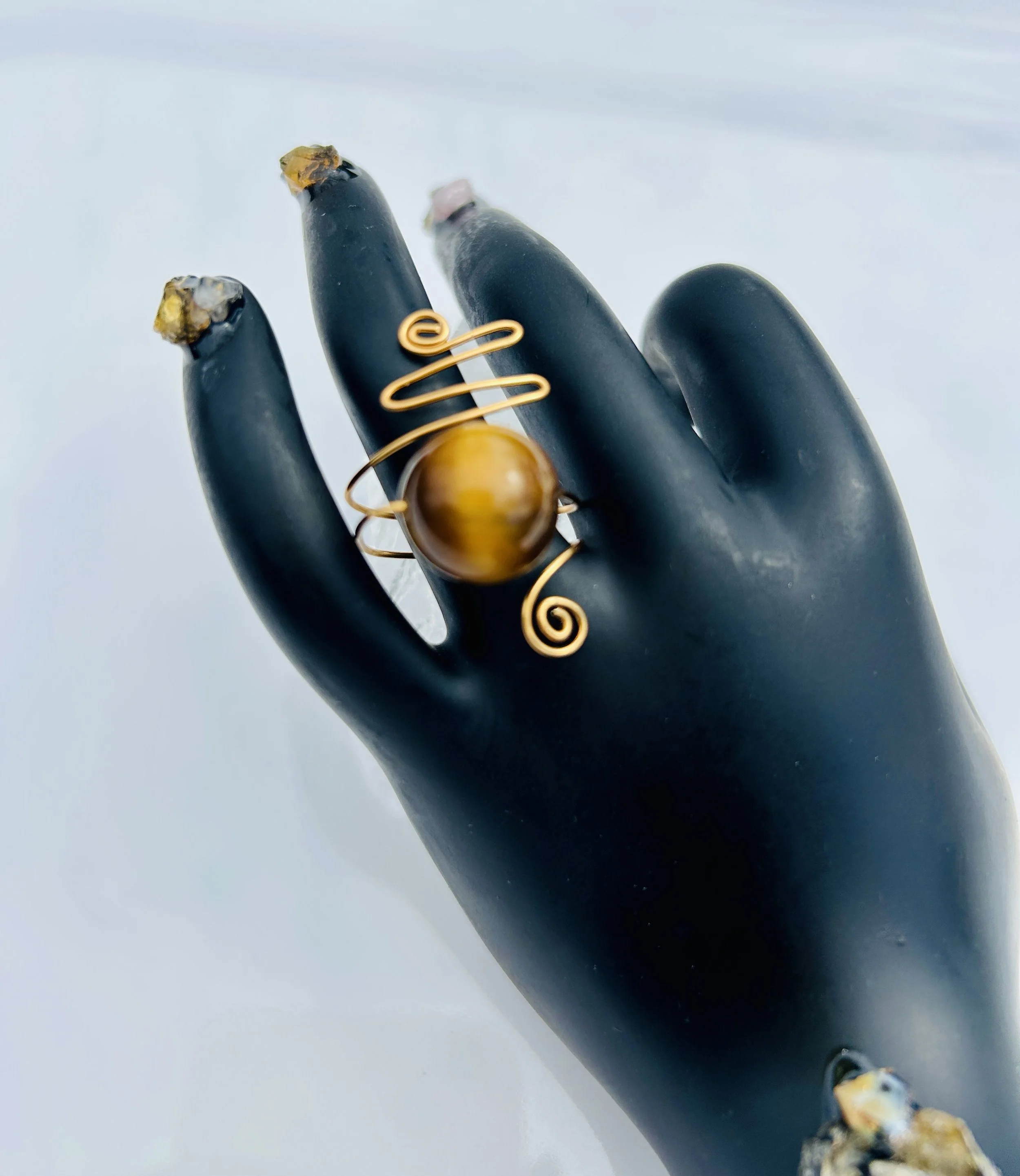 A gold wire ring with a large, round, amber-colored bead is displayed on a black mannequin hand.
