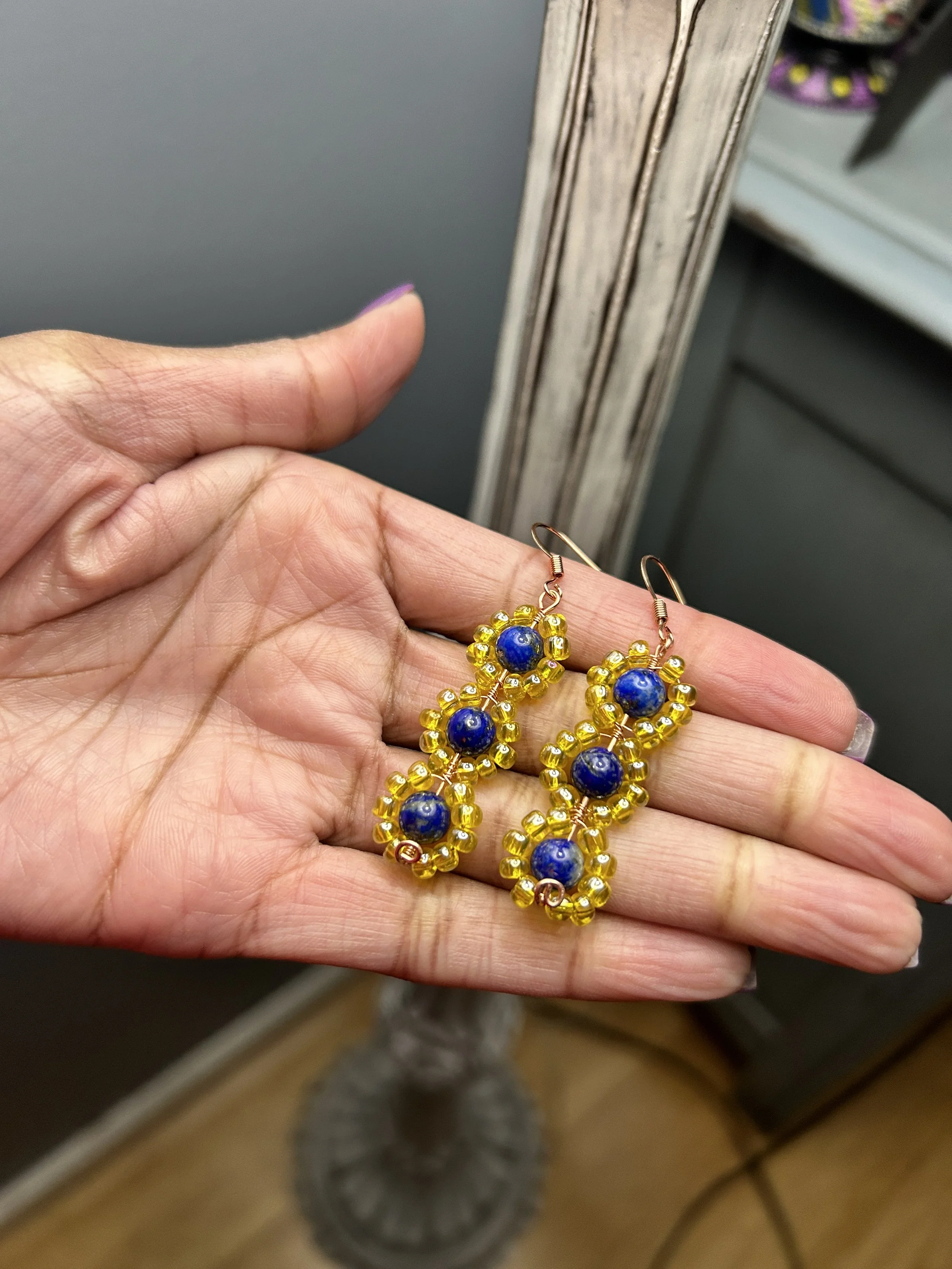 Hand holding a pair of beaded earrings with yellow and blue beads.