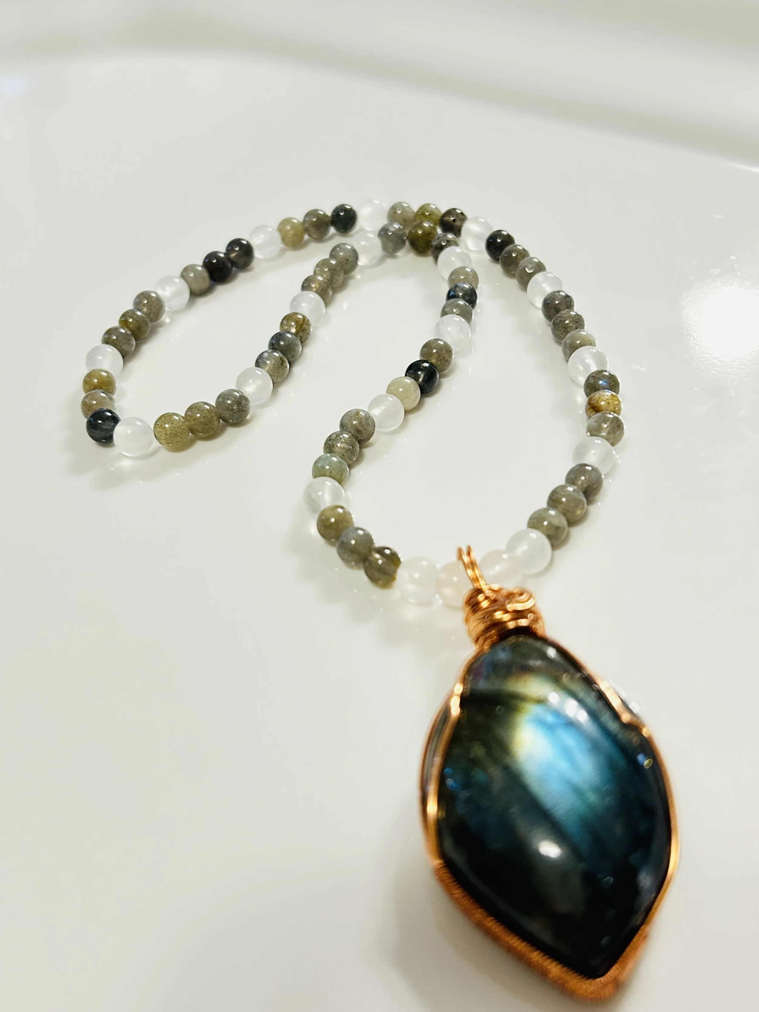 A beaded necklace with a large oval-shaped pendant resting on a white surface.
