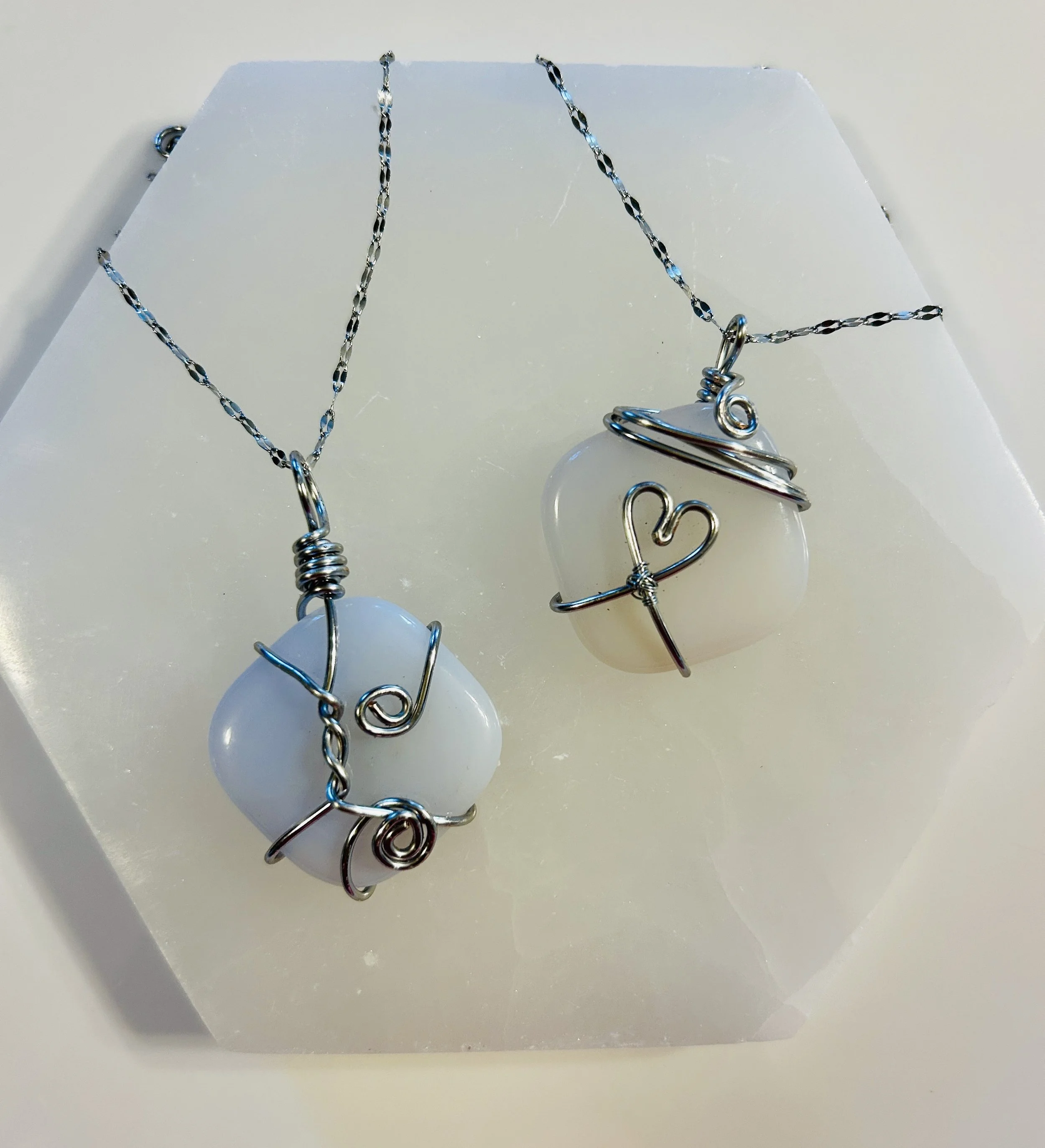 Two necklaces with white stones wrapped in silver wire, each featuring a wireheart charm, displayed on a white surface.