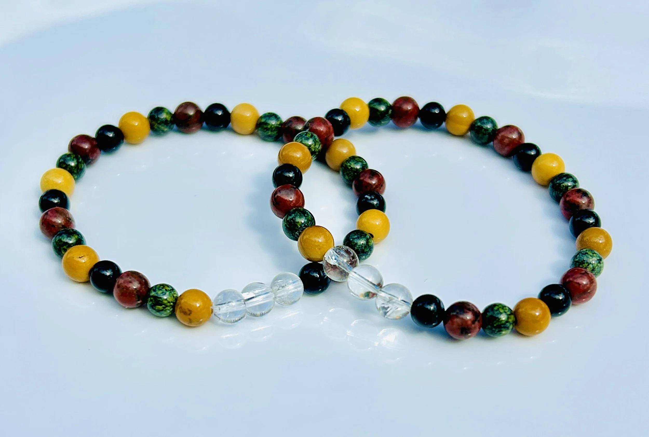 Colorful beaded bracelets on a white surface, featuring green, red, yellow, black, and clear beads.