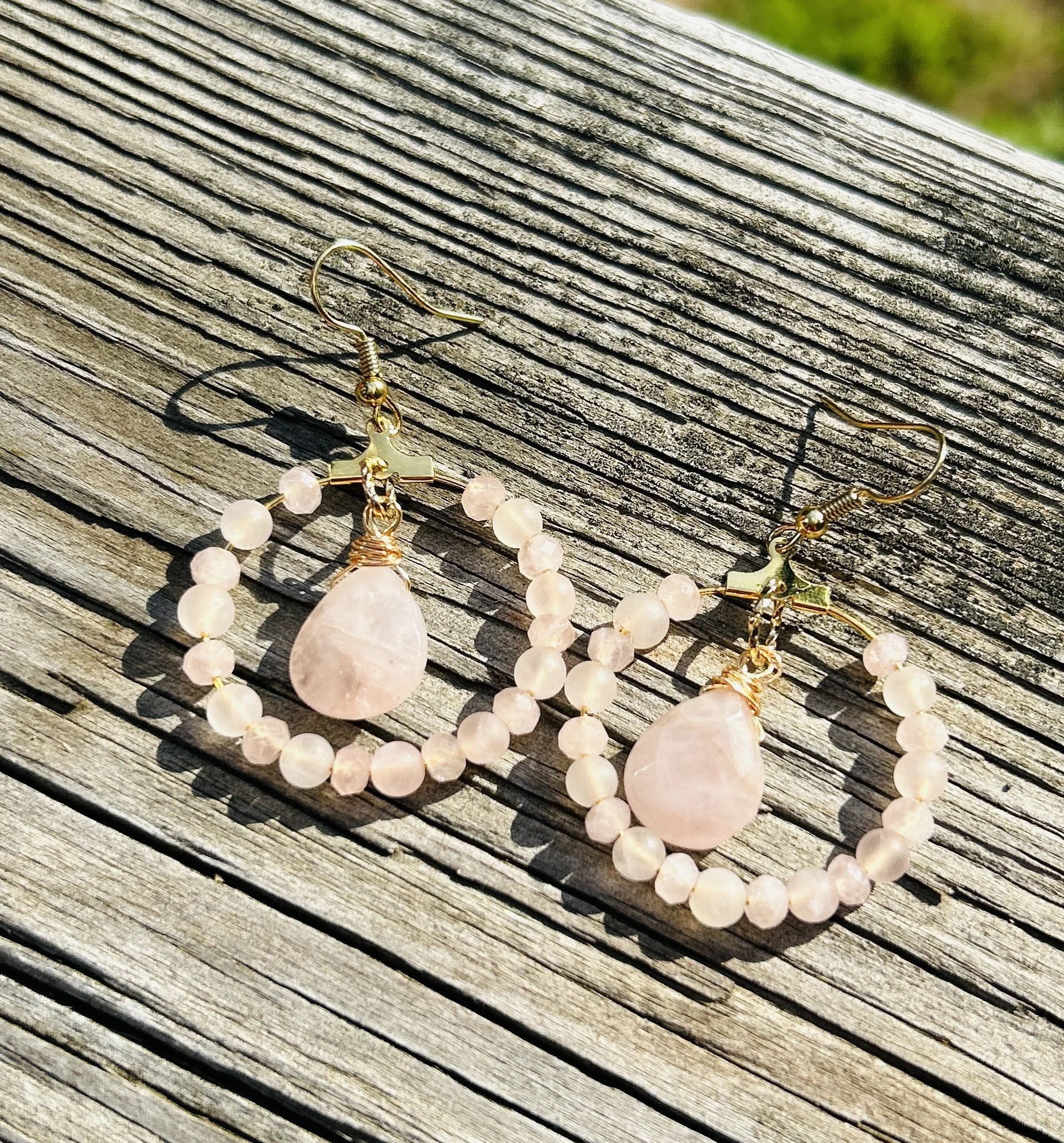 Pink oval gemstone earrings with pink bead frames, laid on a weathered wooden surface.