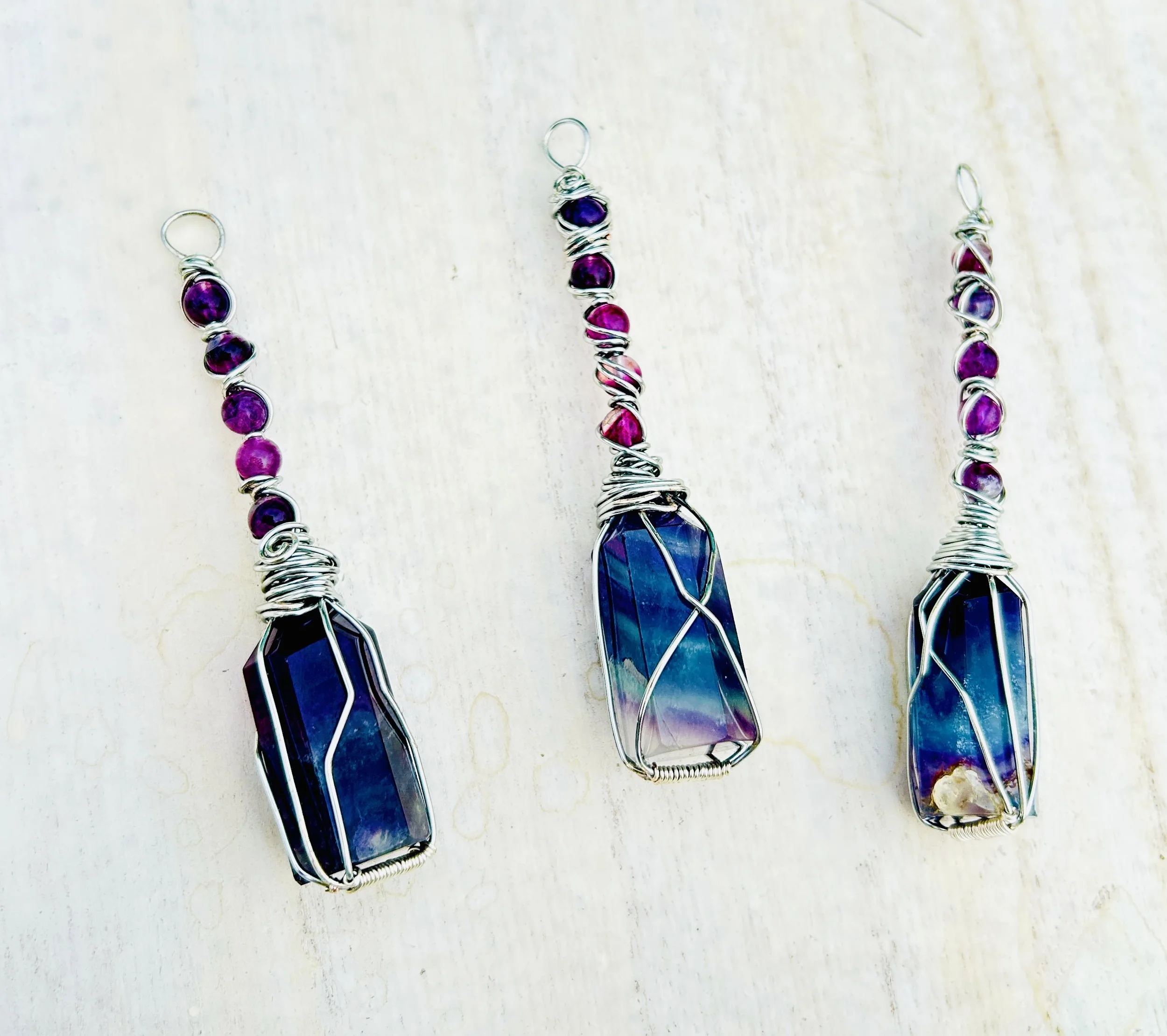 Three wire-wrapped jewelry pieces with large blue and purple stones and pink beads