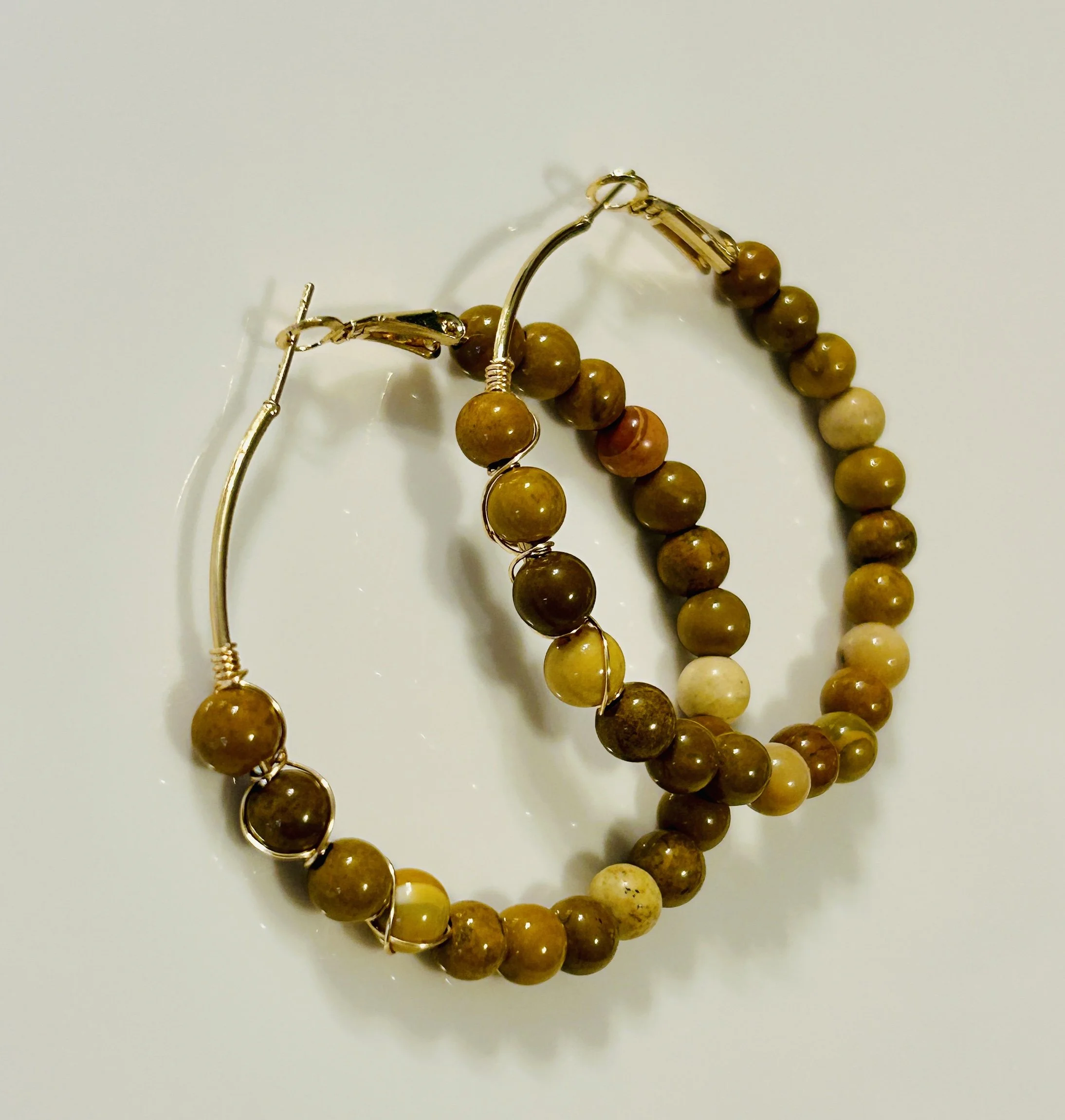 Beige and brown beaded earrings with gold hooks on a white surface.