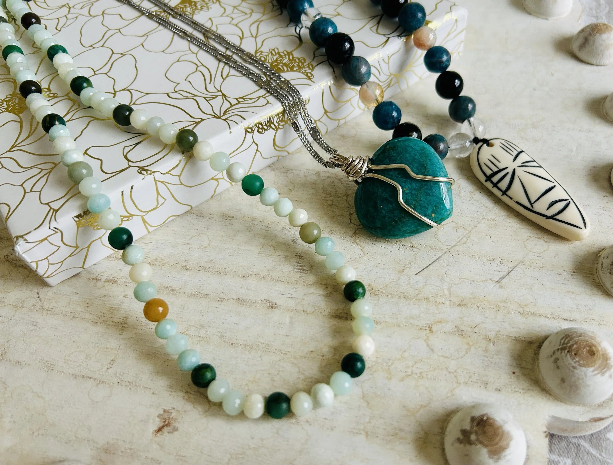 Collection of beaded necklaces and jewelry with shells on a light wooden surface.